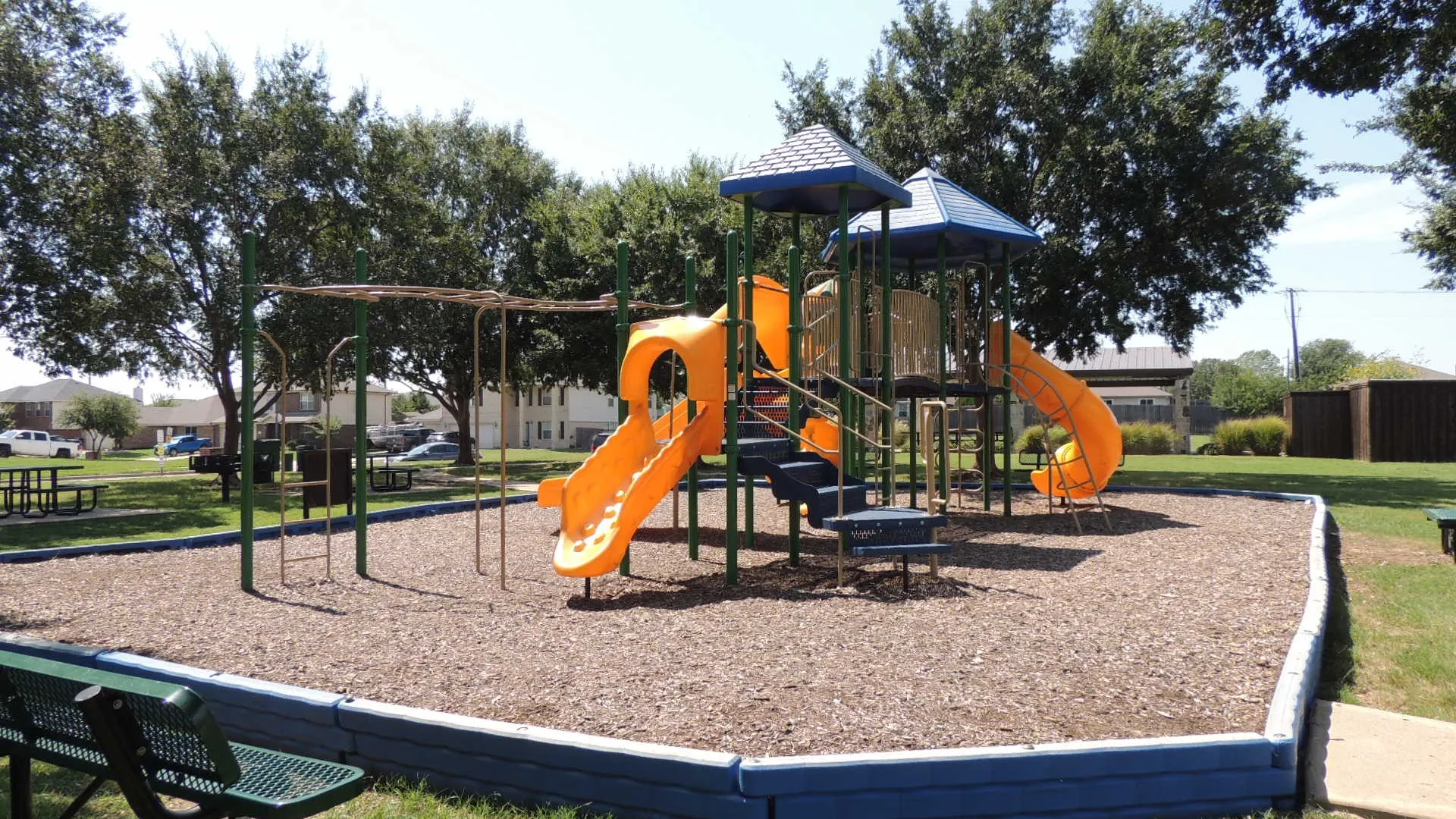 Playground area featuring a multi-level structure with slides, monkey bars, and a wood chip base