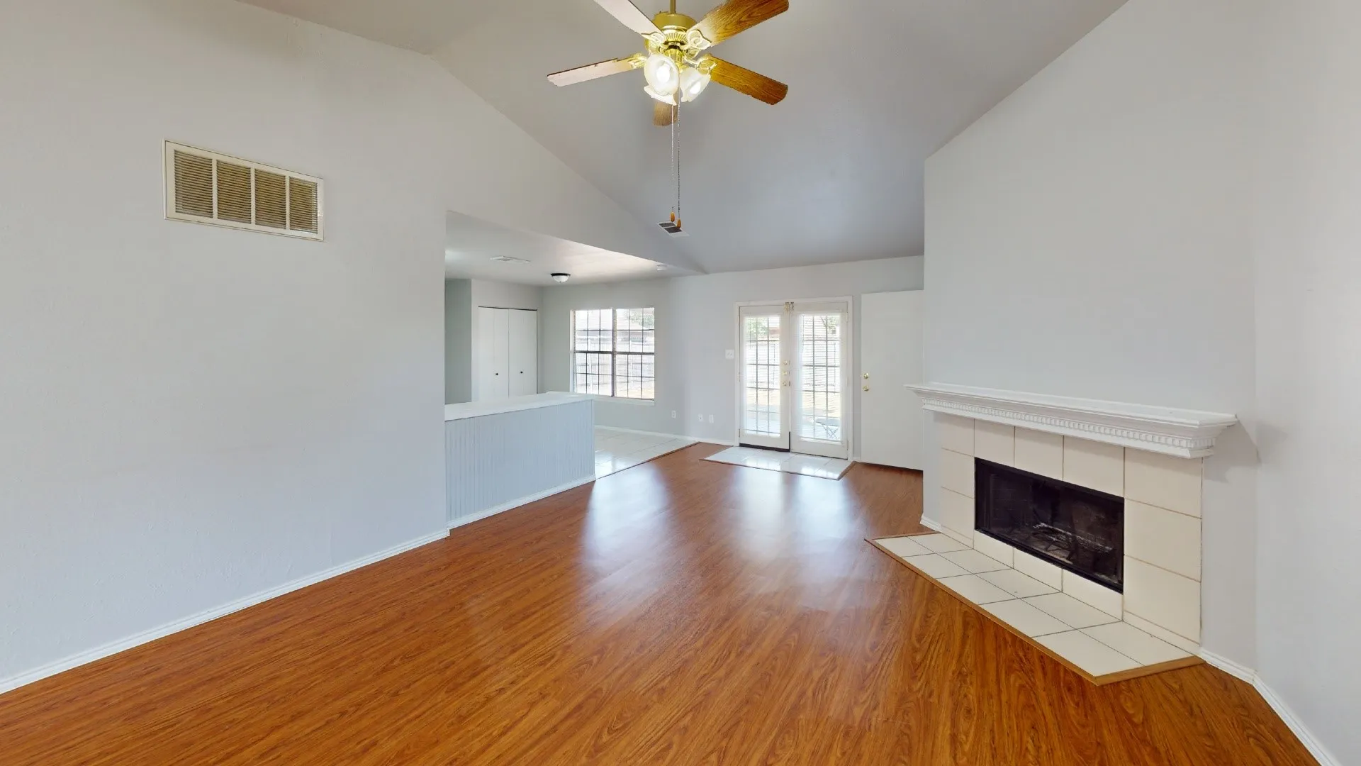 Vaulted ceiling, wood-finish flooring, white tile fireplace, ceiling fan, and French doors
