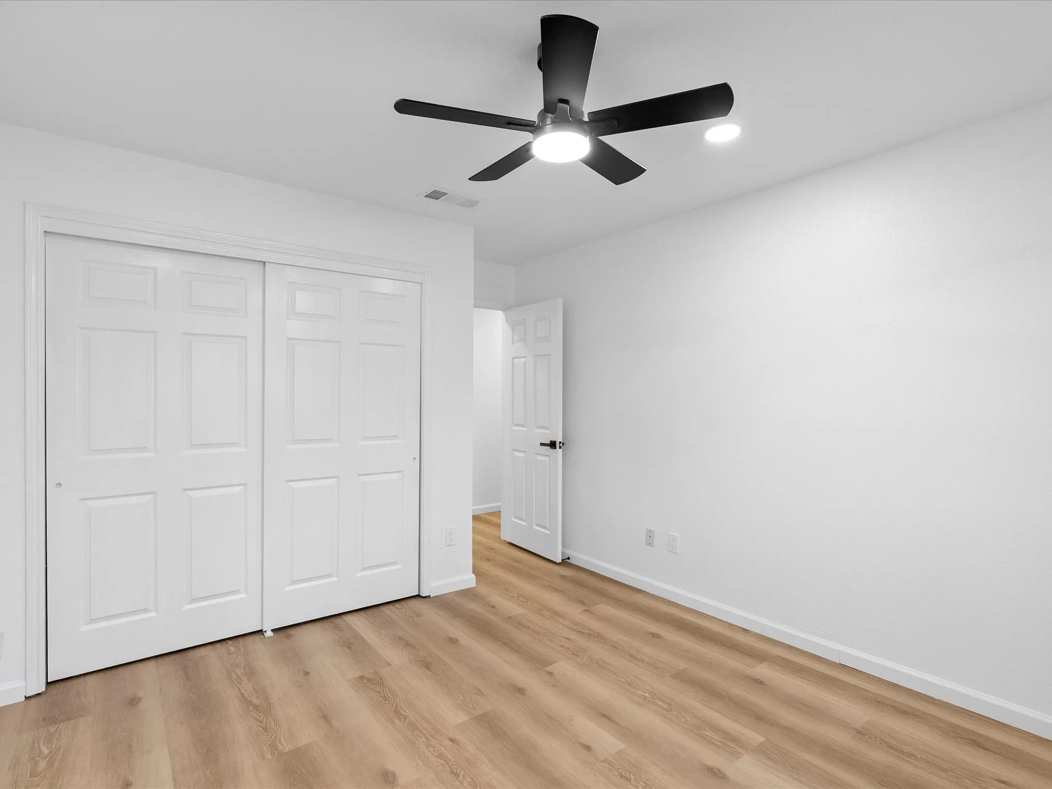 Wood-finish flooring, white walls, white paneled doors, and a black ceiling fan with integrated lighting