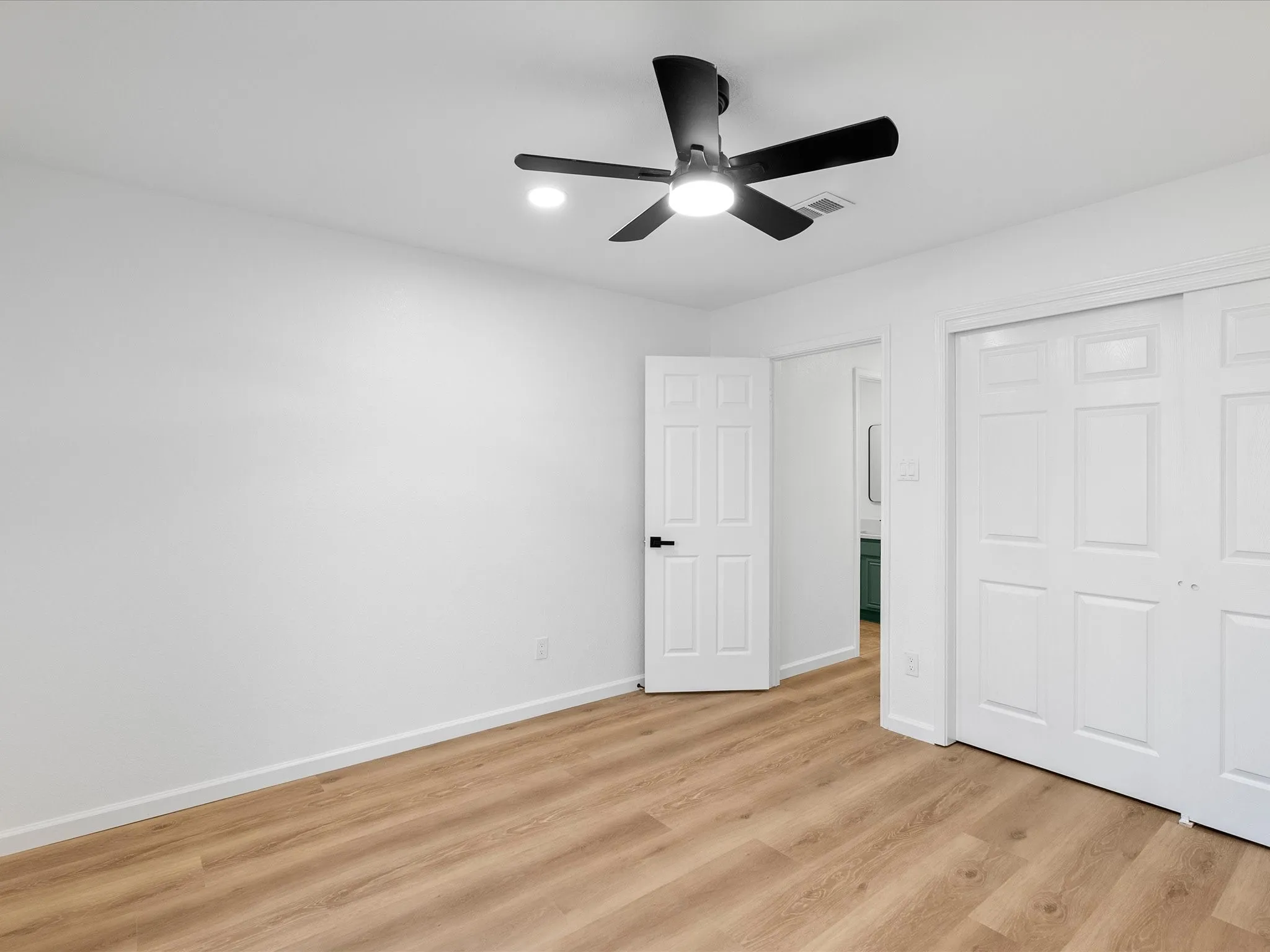 Wood-finish flooring, white walls, and a black ceiling fan with integrated lighting
