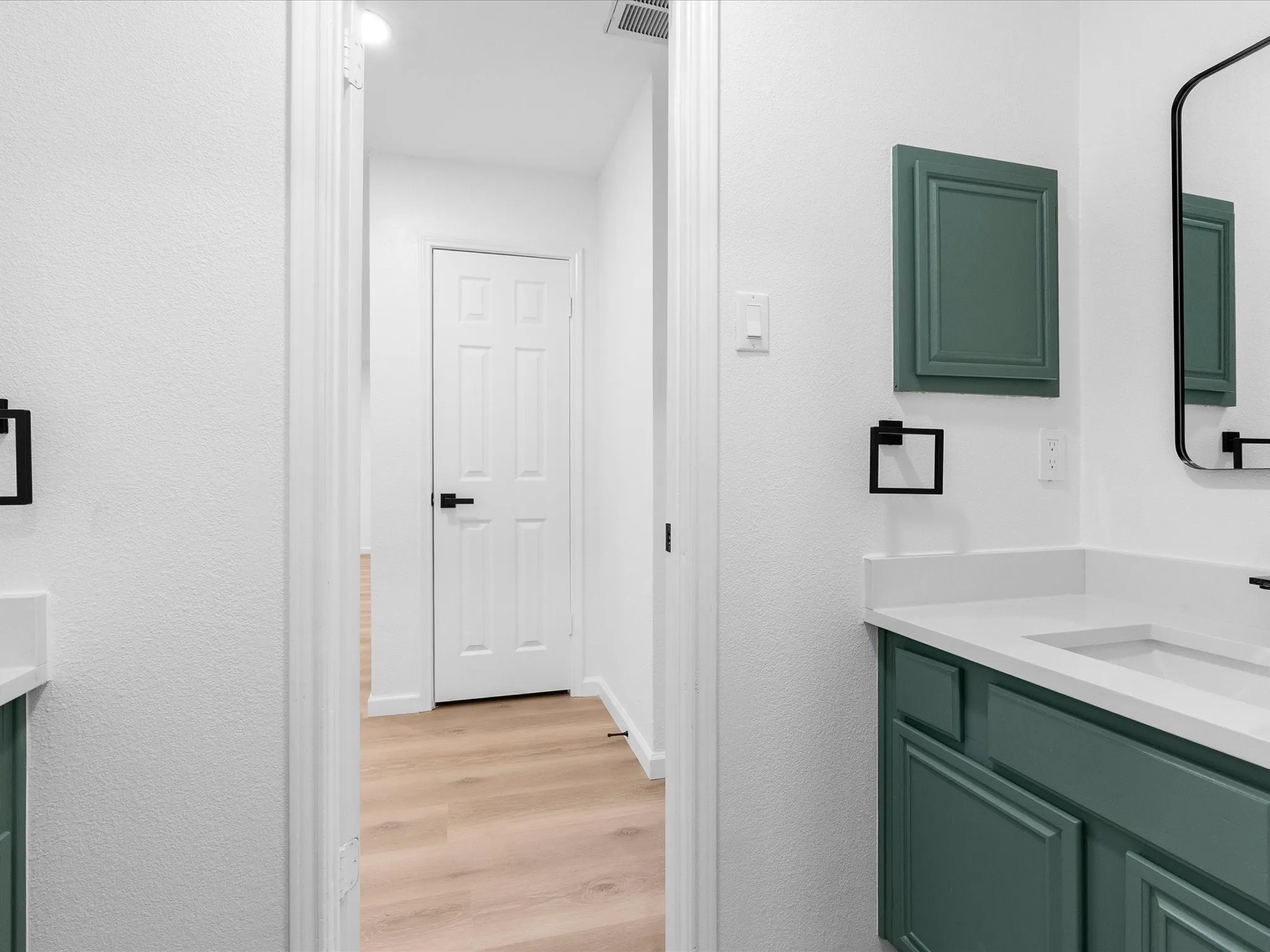 Dual vanity with white countertops and teal cabinetry, featuring integrated sinks and black hardware