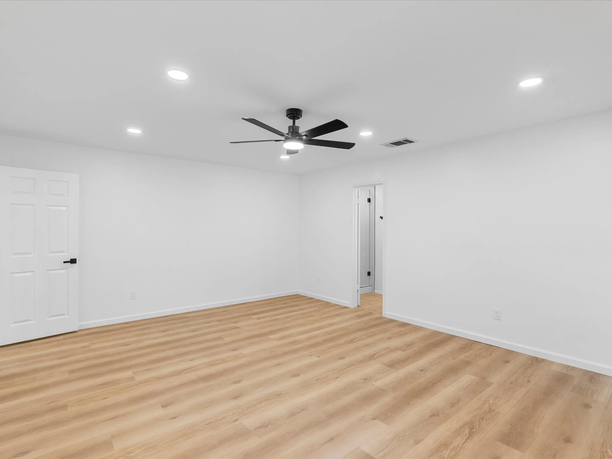 Spacious room with wood-finish flooring, recessed ceiling lighting, a modern ceiling fan, and white paneled doors