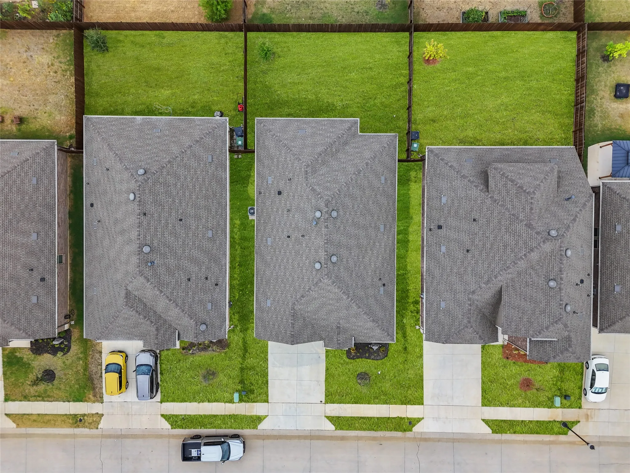 Pitched shingle roof, paved driveway, concrete sidewalk, fenced backyard, and green lawn