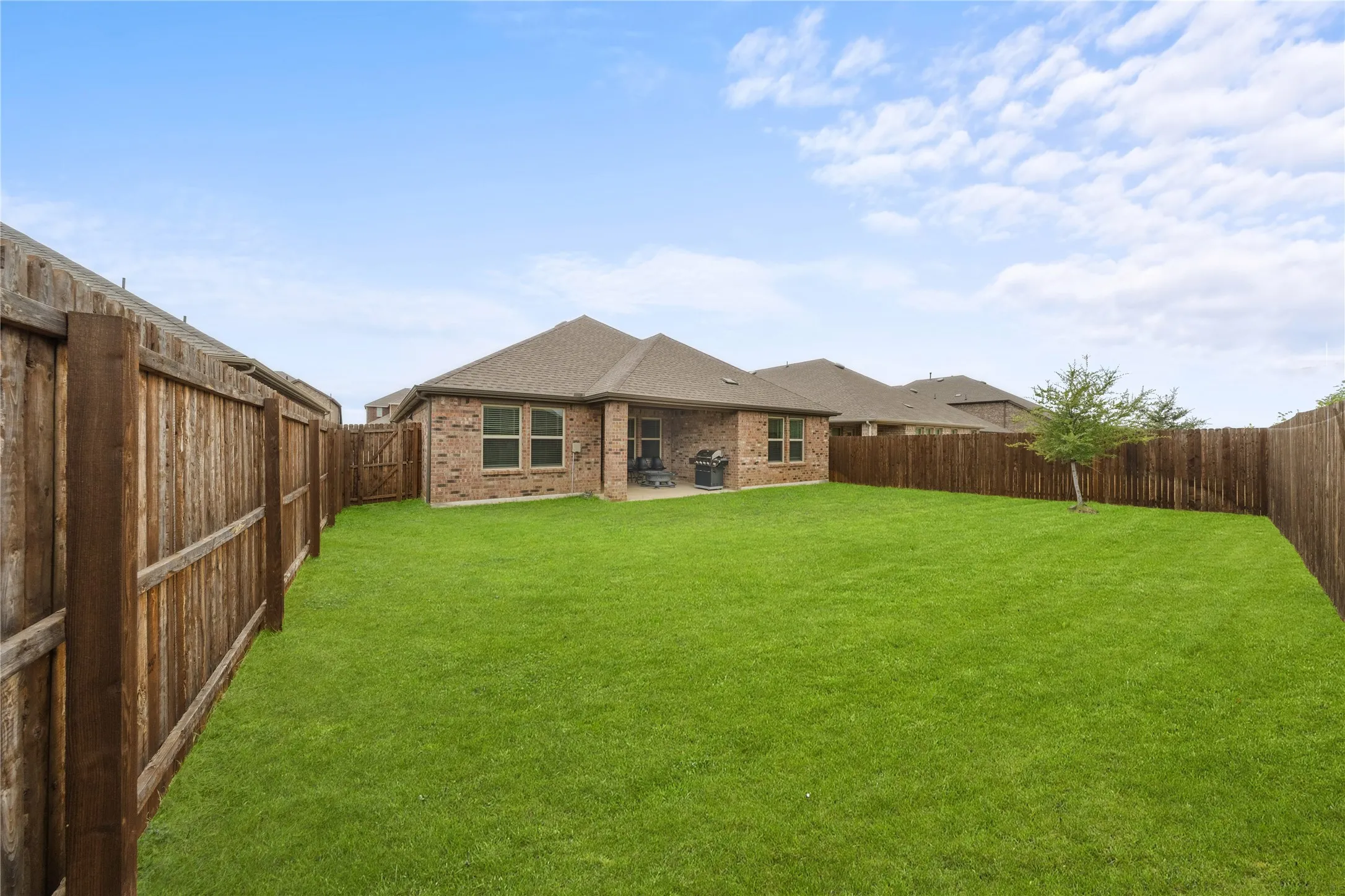 Expansive backyard featuring a manicured lawn, full privacy fencing, and a brick-clad exterior