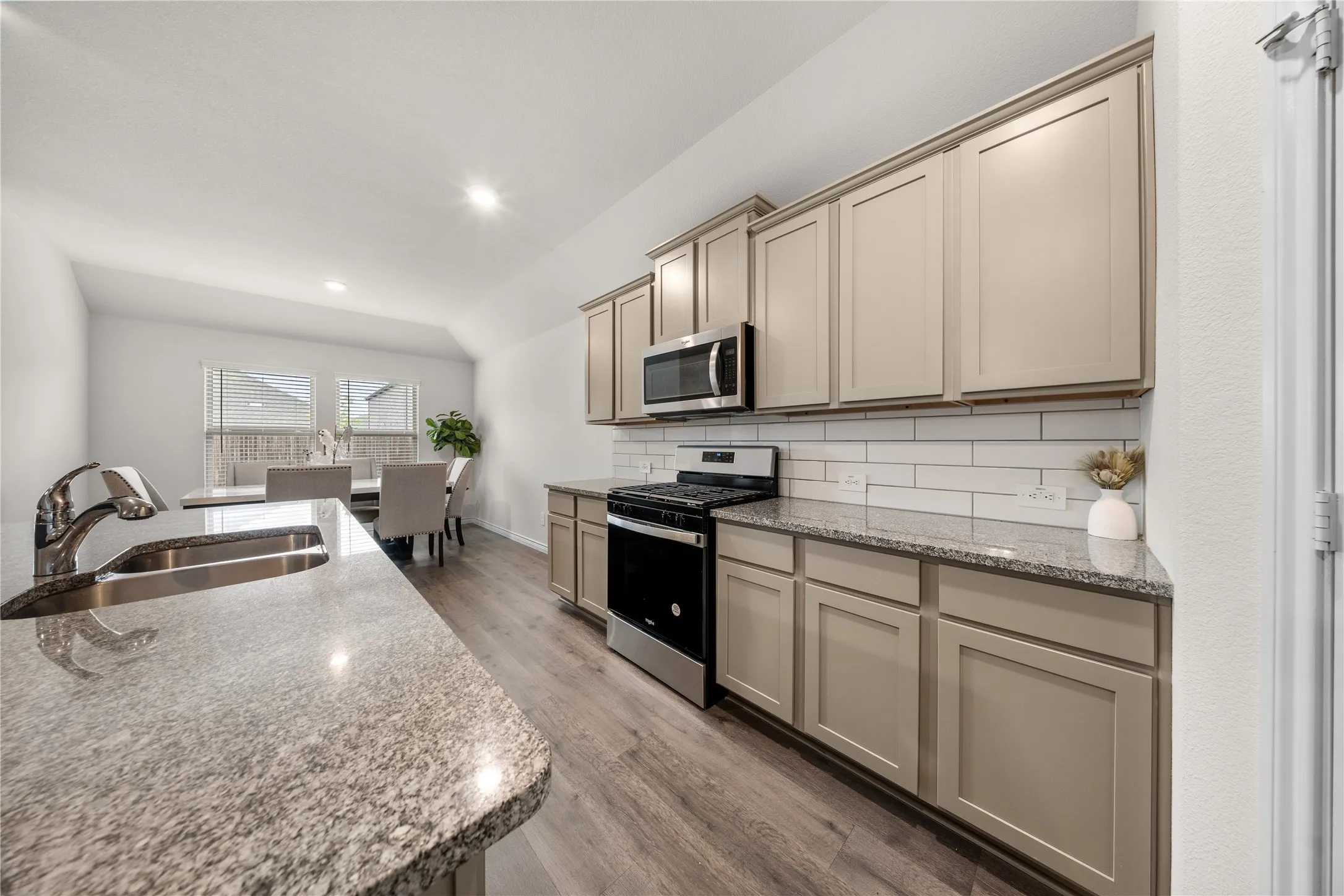 Kitchen featuring granite countertops, stainless steel appliances, white subway tile backsplash, recessed lighting, and wood-finish flooring