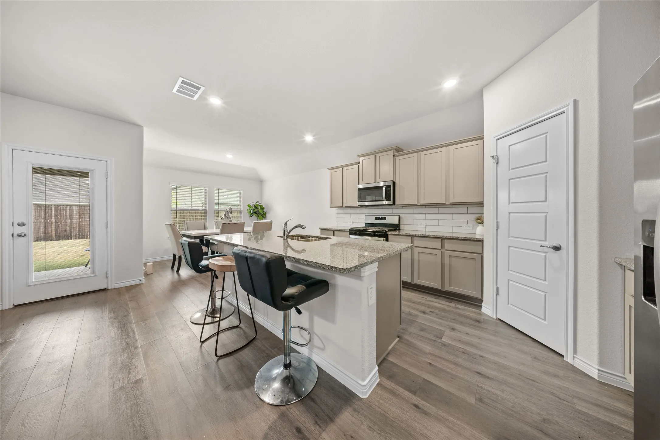 Kitchen featuring wood-finish flooring, an island with granite countertops, stainless steel appliances, and light-toned cabinetry