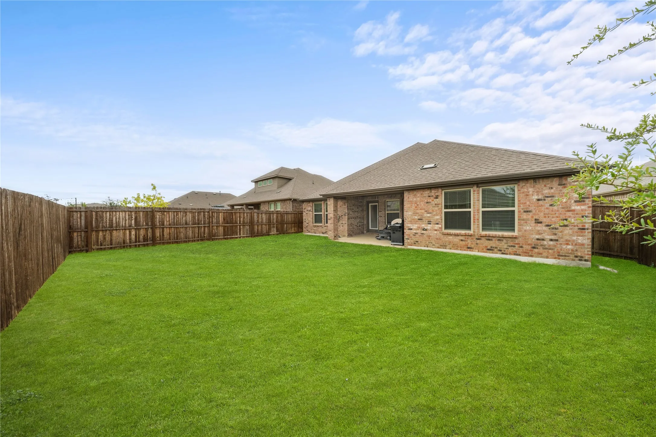 Expansive fenced yard with a manicured lawn, brick exterior, covered patio, and large windows