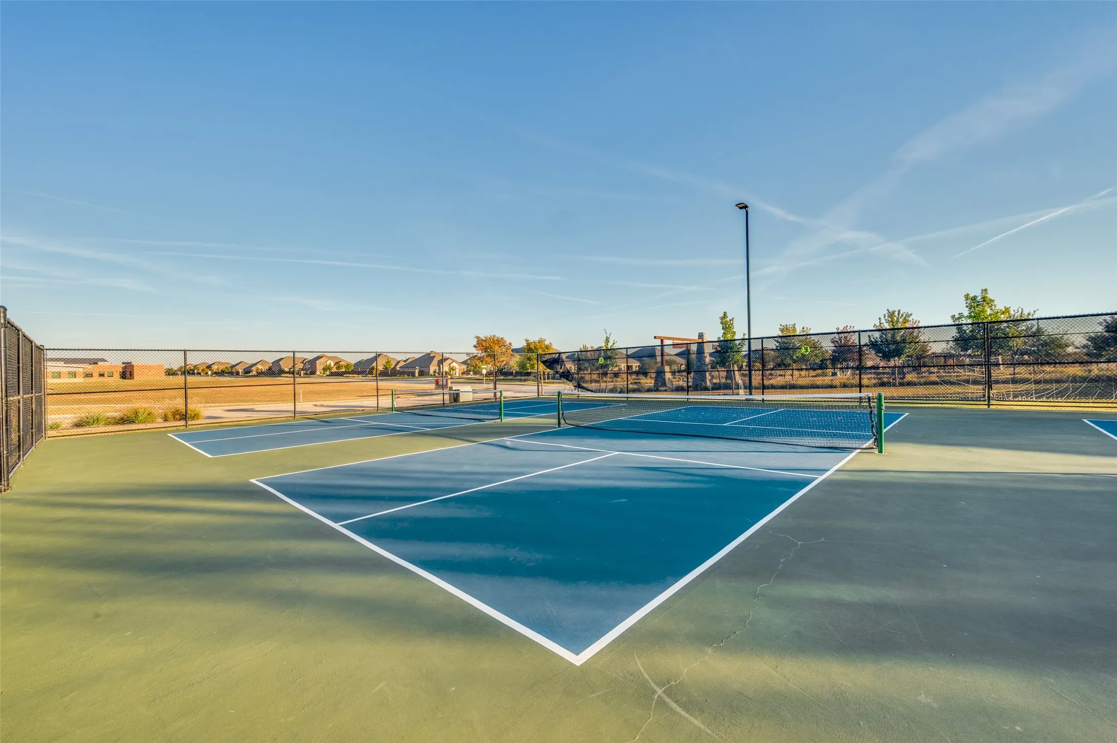 Multiple outdoor courts featuring blue and green surfacing, white line markings, and perimeter fencing