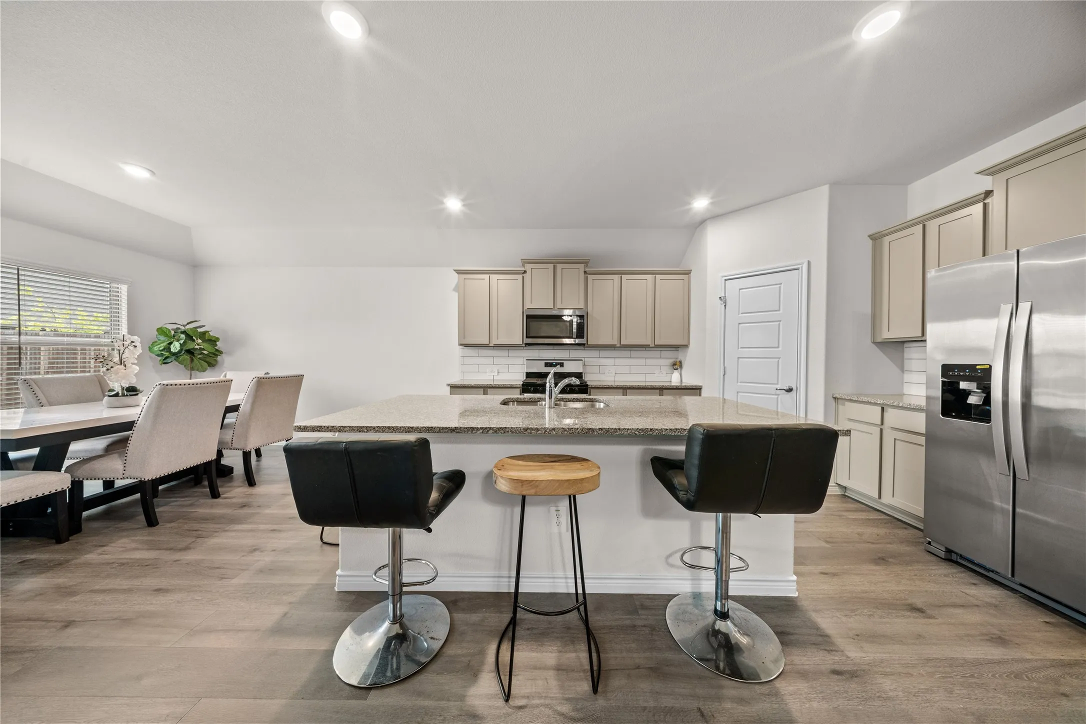 Kitchen featuring light-finish cabinetry, stainless steel appliances, a large center island with a stone countertop, and wood-finish flooring