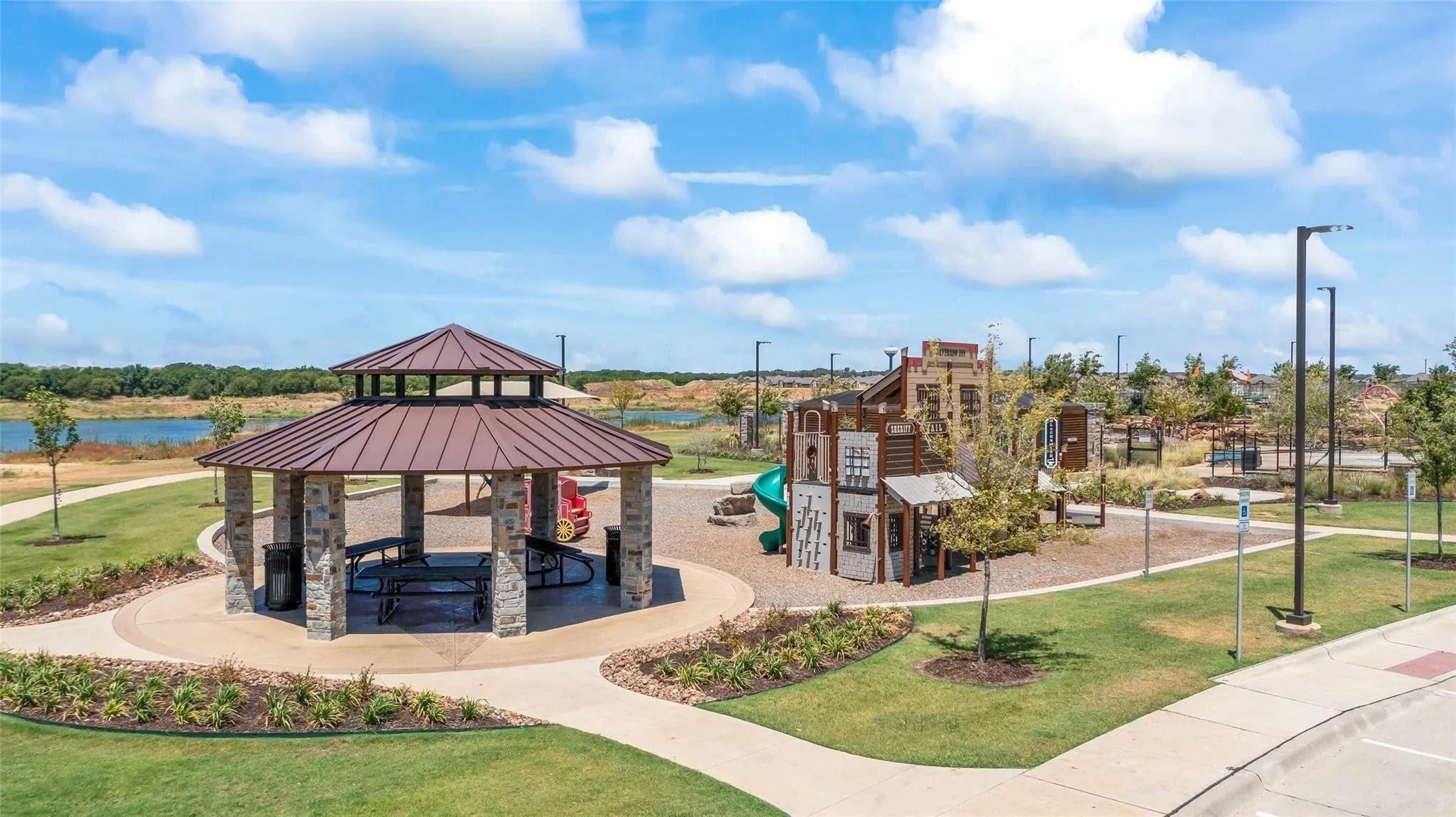 Community recreational area featuring a stone and metal roof gazebo, playground equipment, paved pathways, and manicured green spaces
