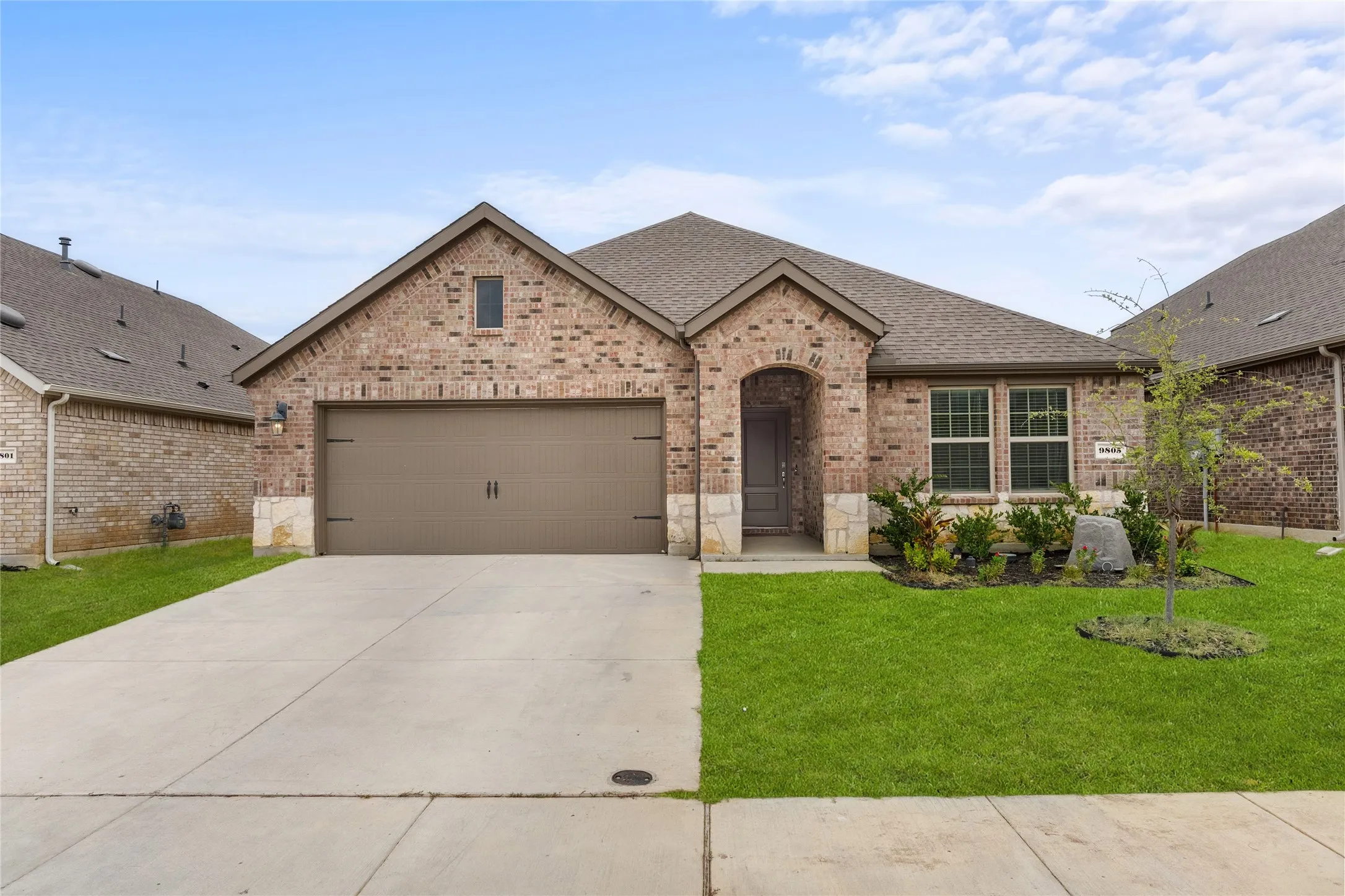 Brick and stone facade with an arched entryway, two-car garage, and concrete driveway