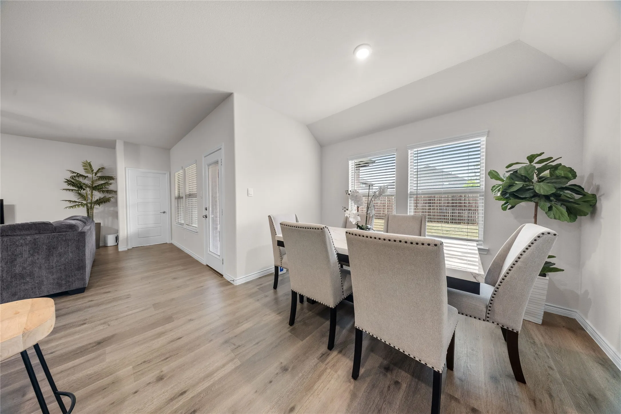 Wood-finish flooring throughout, white interior walls, recessed lighting, multiple windows with blinds, and a white door with glass paneling