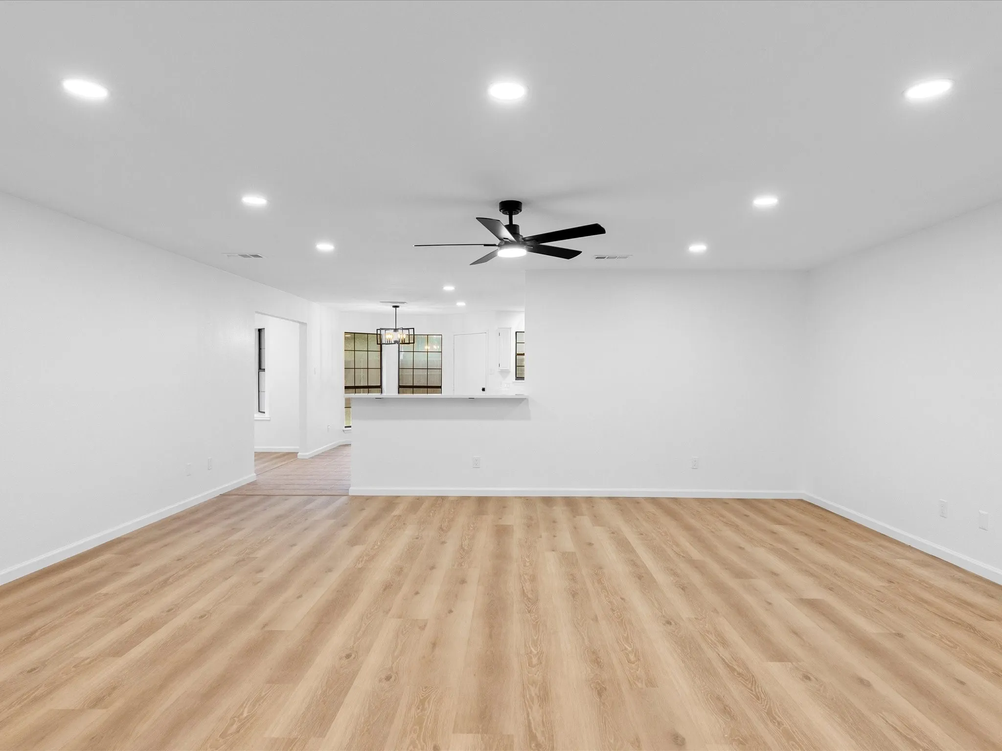 Recessed ceiling lighting, wood-finish flooring, ceiling fan, white wall finishes, and a partial wall with a countertop