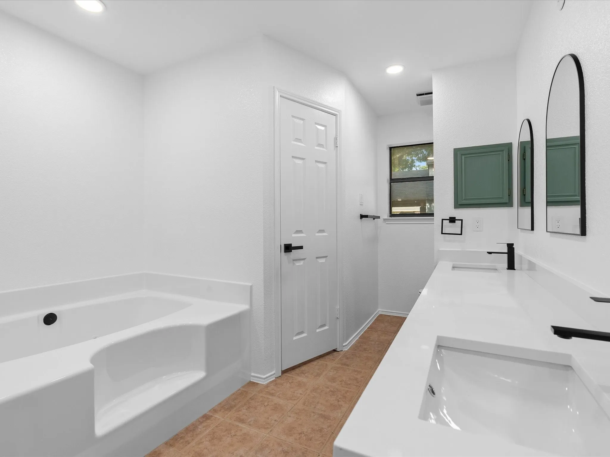 Recessed lighting illuminates a dual-sink vanity with matte black faucets and white countertops