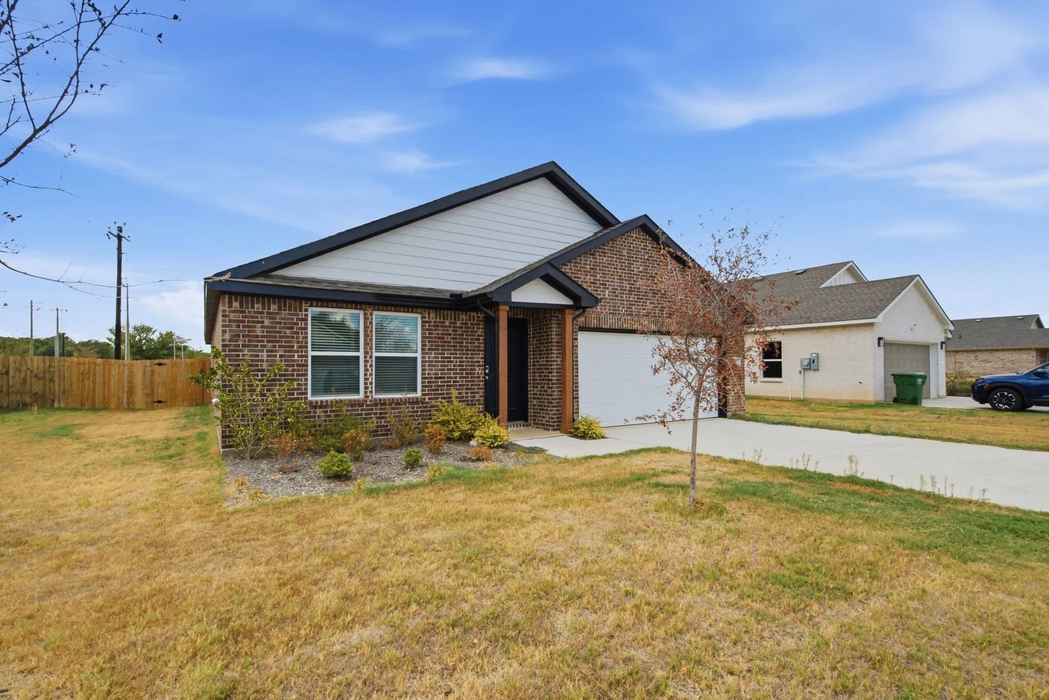Brick and siding exterior with dark trim, attached garage, concrete driveway, and a wood privacy fence