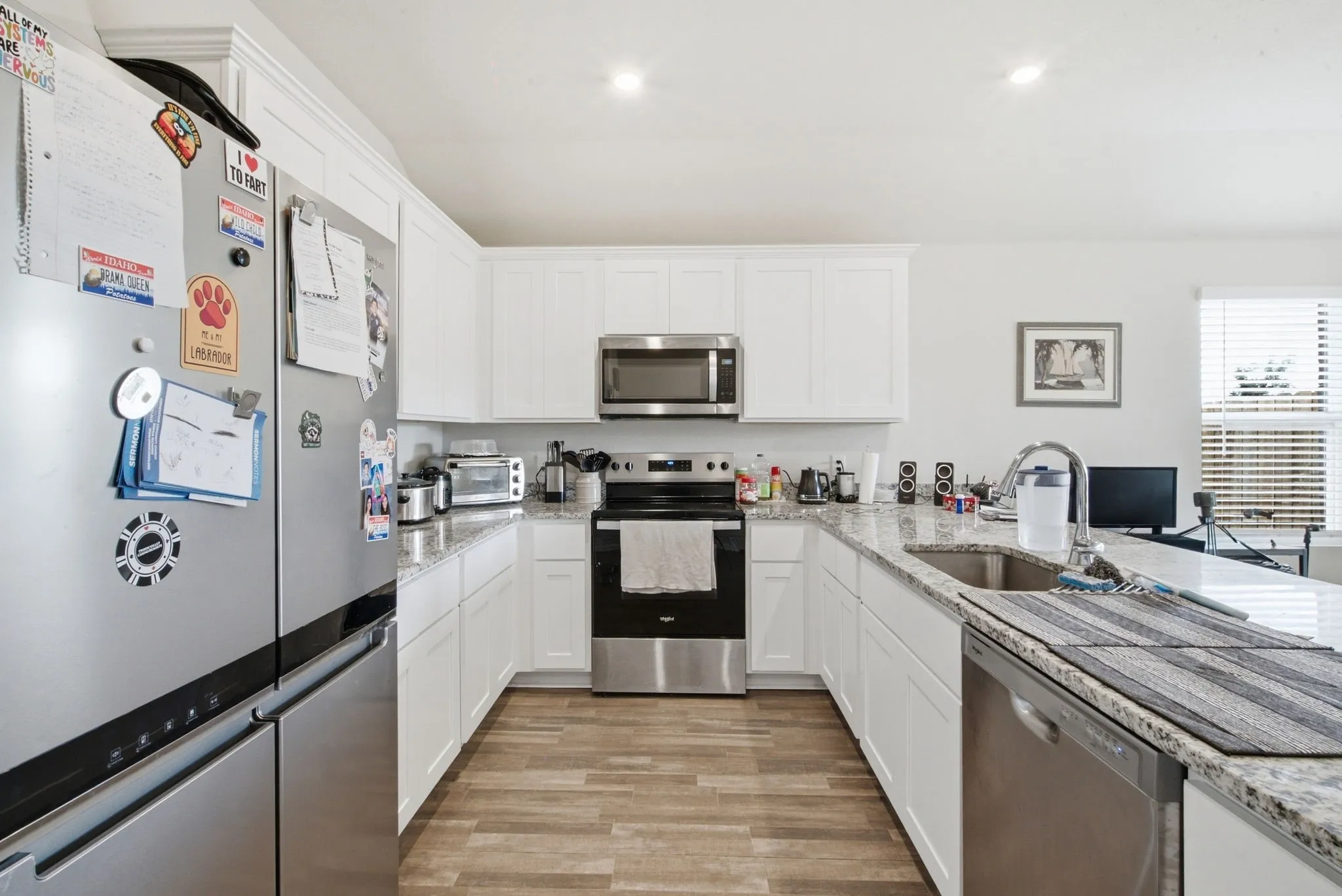 Kitchen featuring white cabinetry, granite countertops, stainless steel appliances, and wood-finish flooring