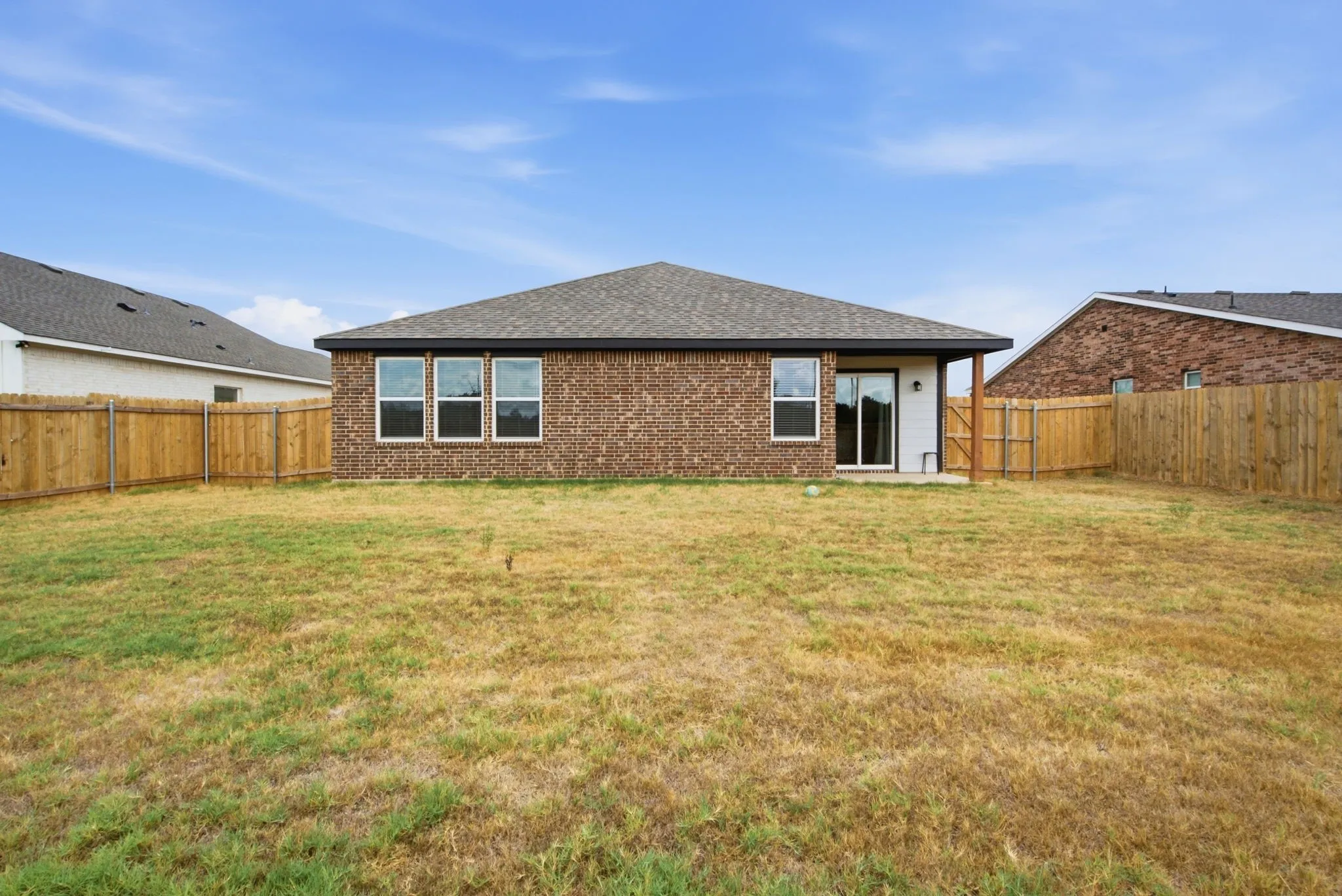 Expansive backyard with a full privacy fence, brick exterior, and covered patio
