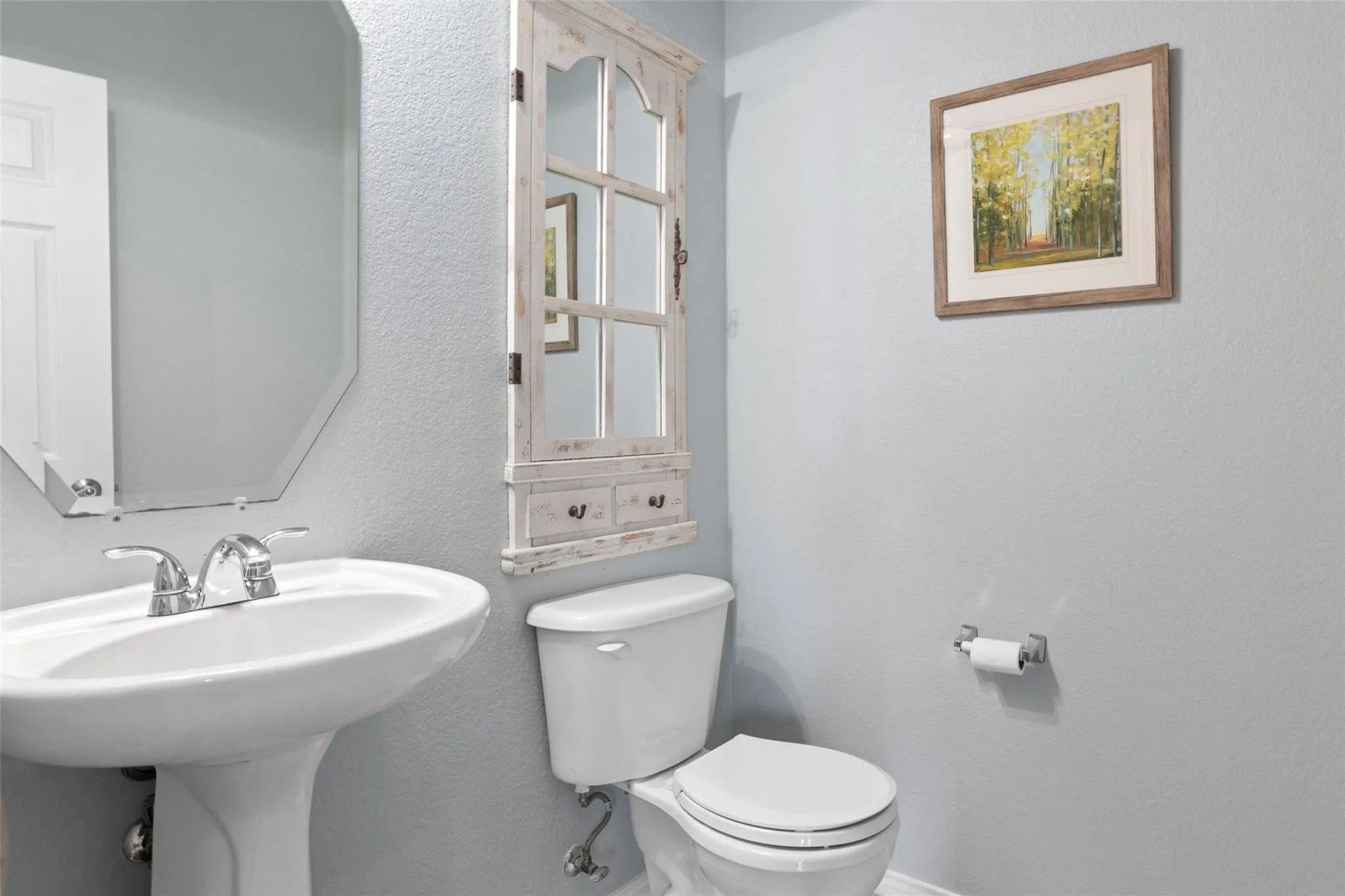 Pedestal sink with chrome faucet, octagonal mirror, built-in storage cabinet with glass-paneled doors, and a toilet