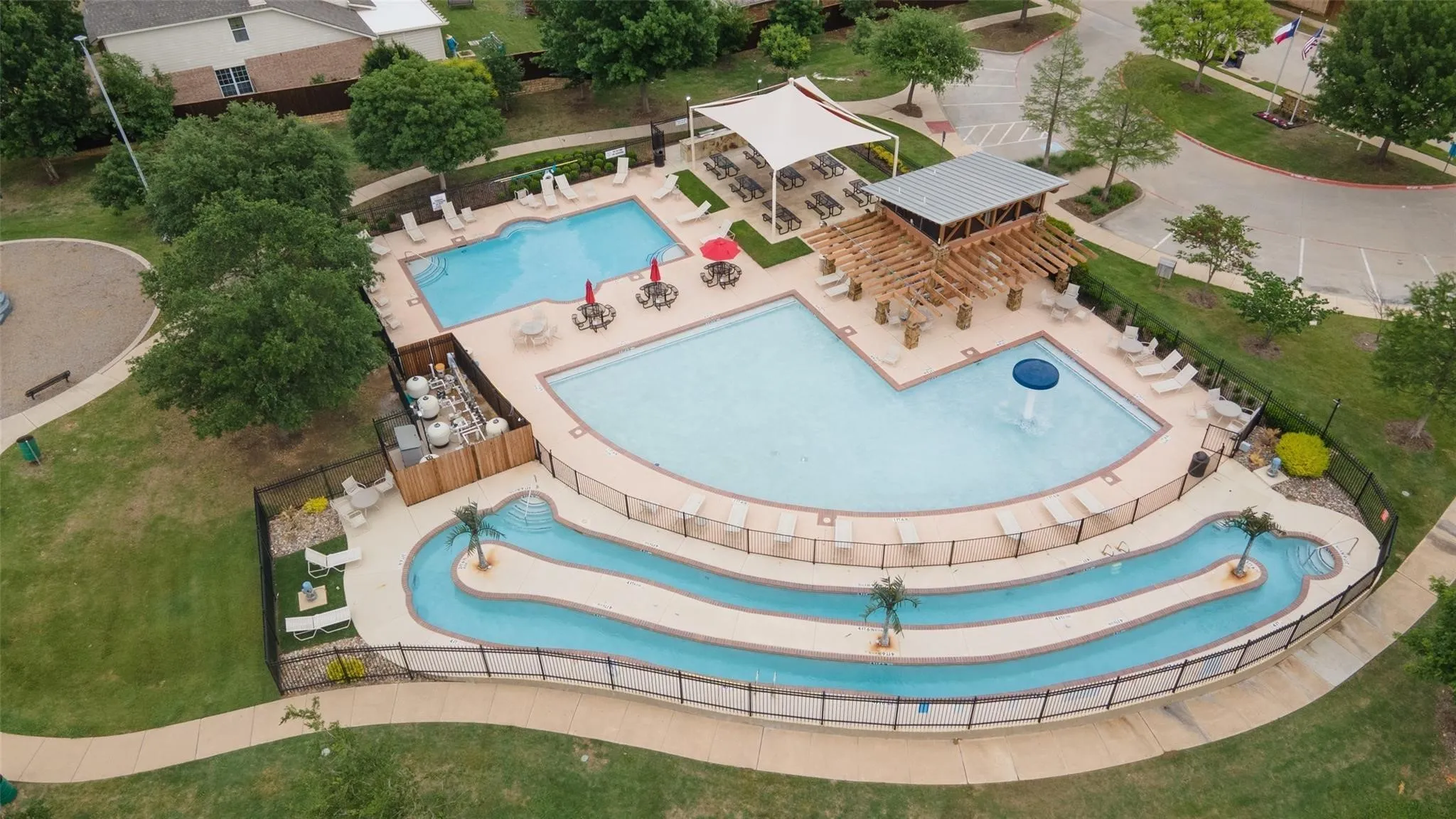 Expansive pool area featuring multiple swimming pools, a winding lazy river, a shaded seating structure, and a dedicated splash feature