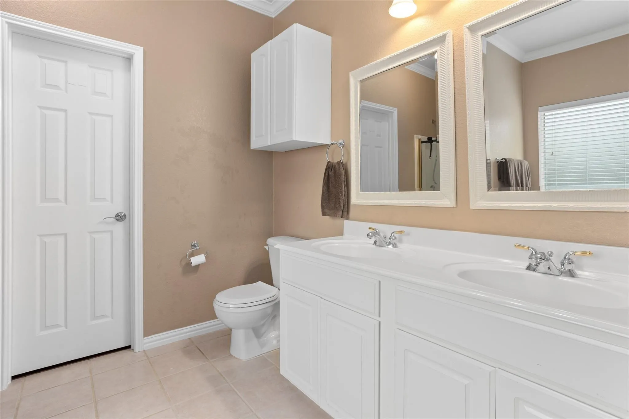 Dual vanity with white cabinetry, framed mirrors, and tile flooring