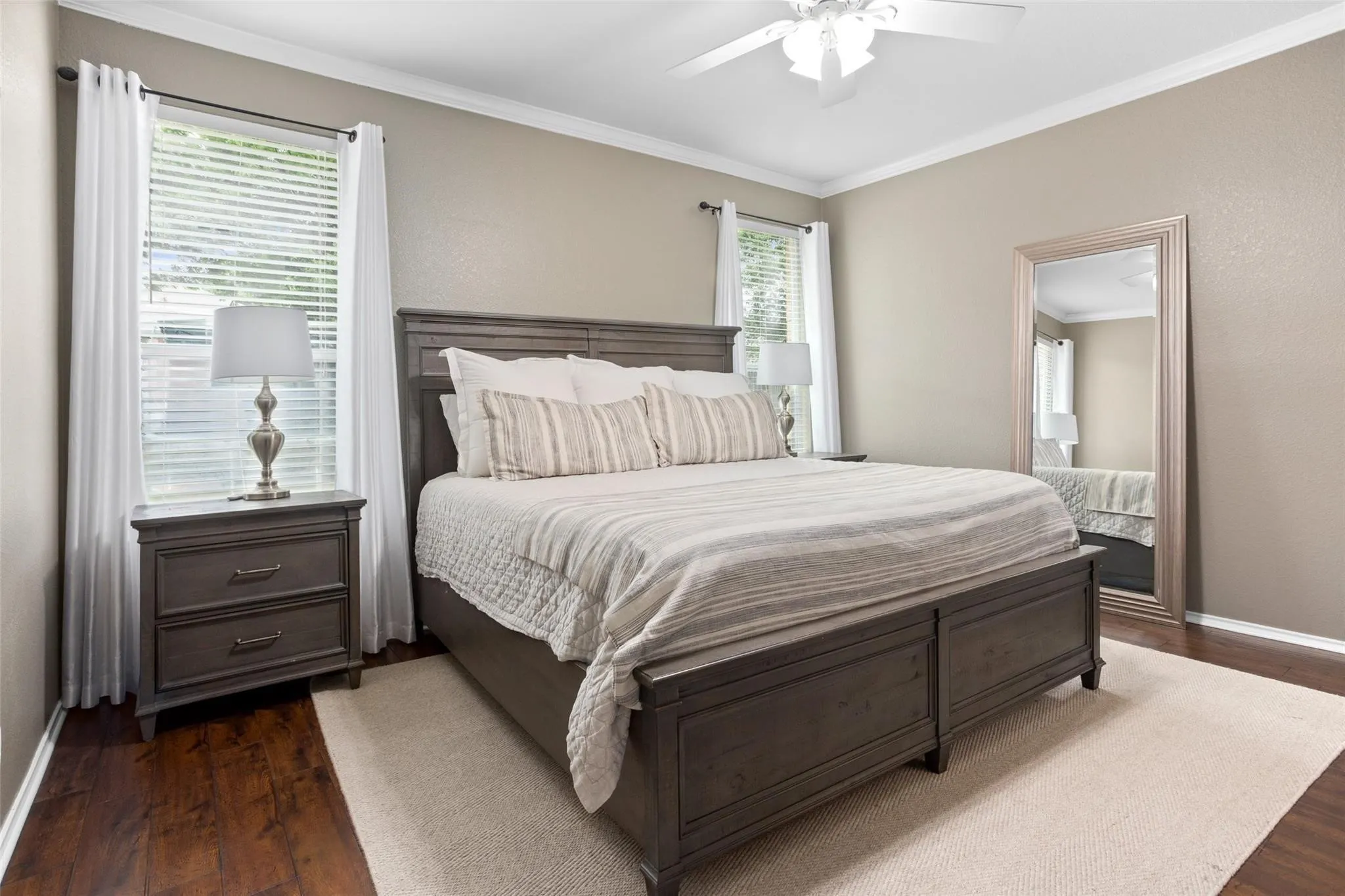 Hardwood-style flooring with white trim, a ceiling fan, and multiple windows with blinds