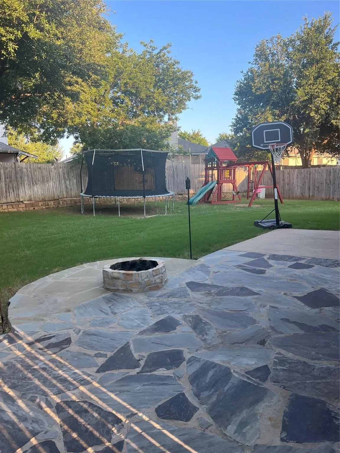 Expansive flagstone patio with a built-in stone fire pit, bordered by a manicured lawn and a privacy fence