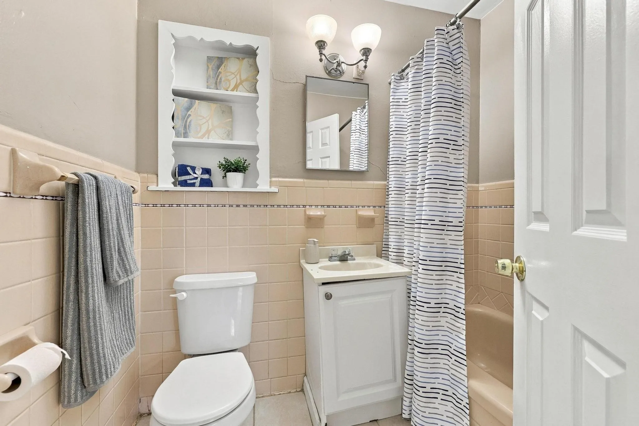 Built-in shelving, vanity with integrated sink, wall-mounted lighting fixture, full bathtub, and tiled walls