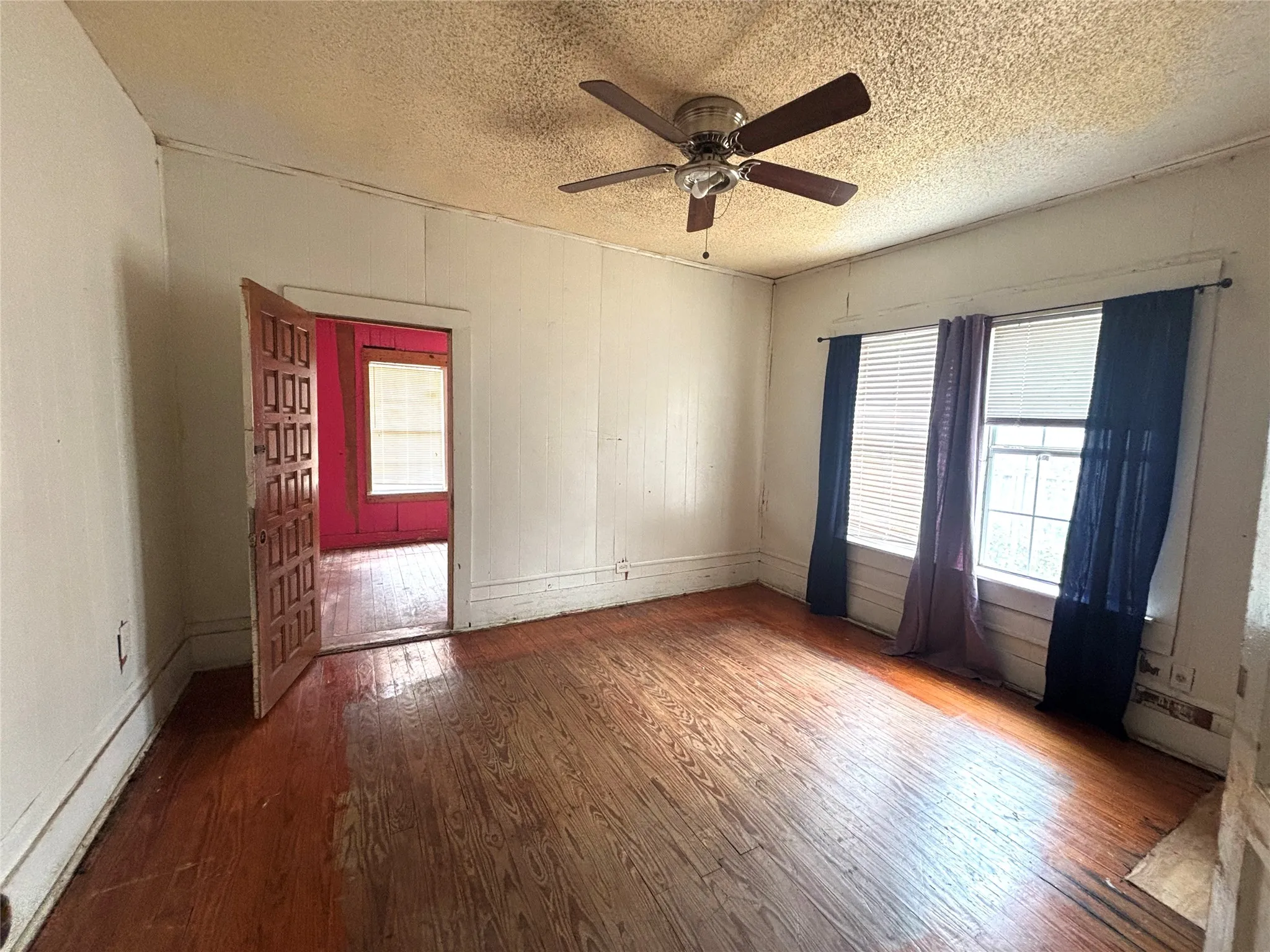 Wood-finish flooring, wood paneling, ceiling fan with light fixture, and paneled interior door