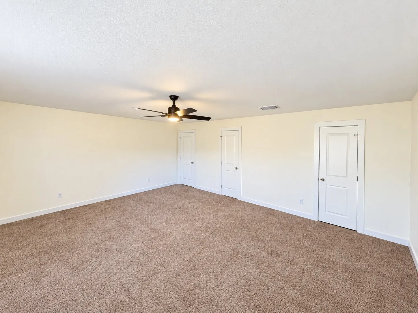 Spacious room with plush carpet flooring, a ceiling fan with integrated lighting, and multiple interior doors