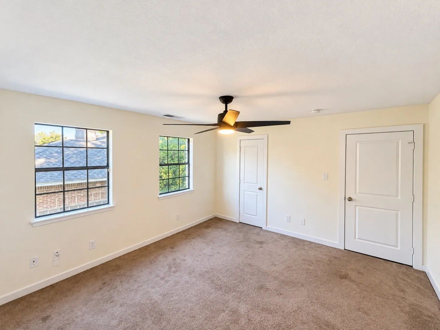 Expansive room featuring two windows with grids, neutral carpet flooring, a ceiling fan with integrated lighting, and two panel doors