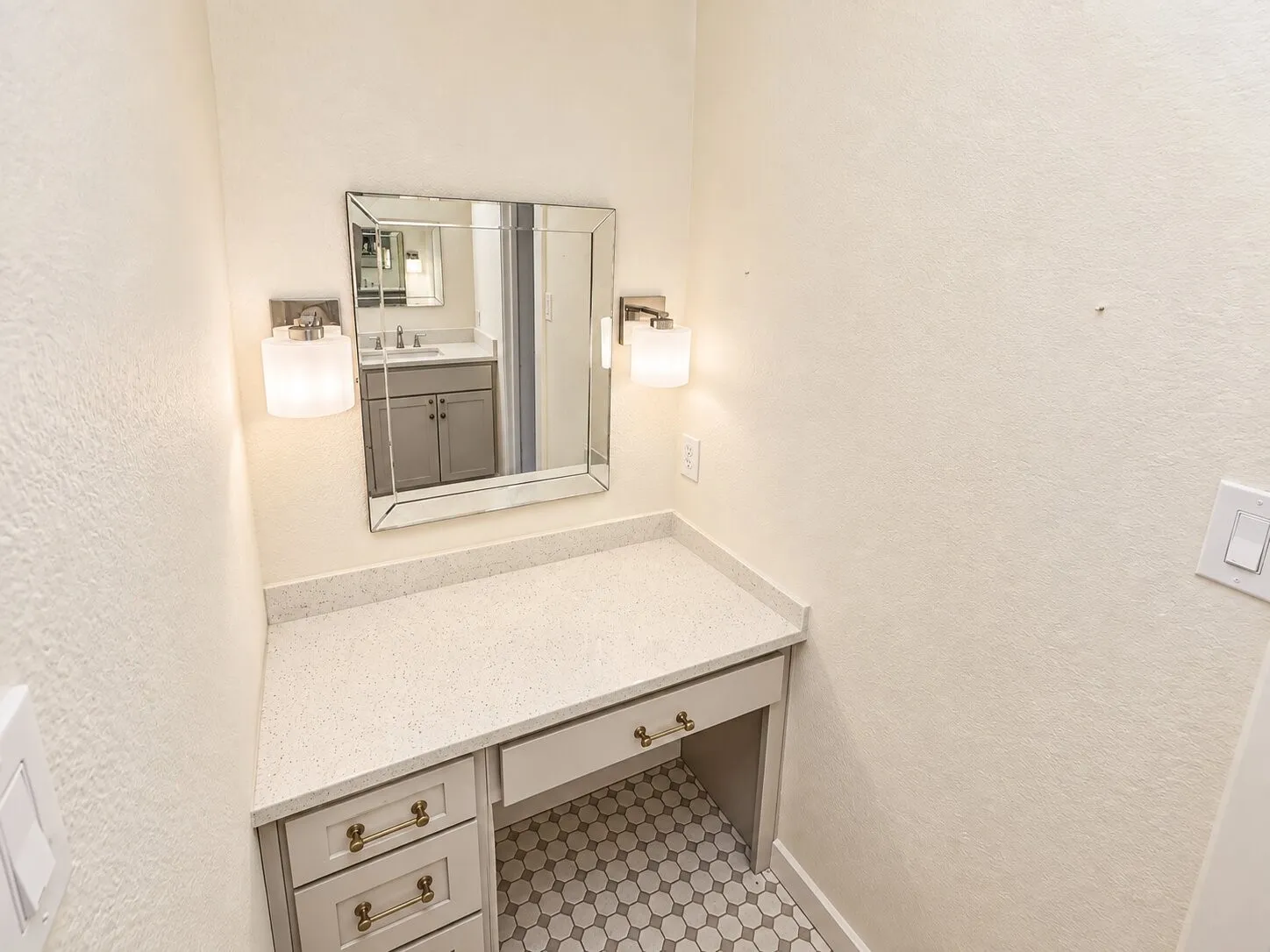 Built-in vanity with a speckled countertop, gray cabinetry, and brass hardware