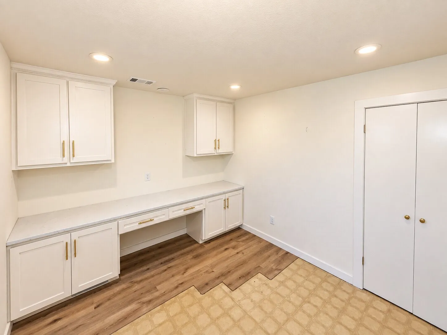 Built-in desk with white cabinetry, light-toned countertops, and gold-tone hardware