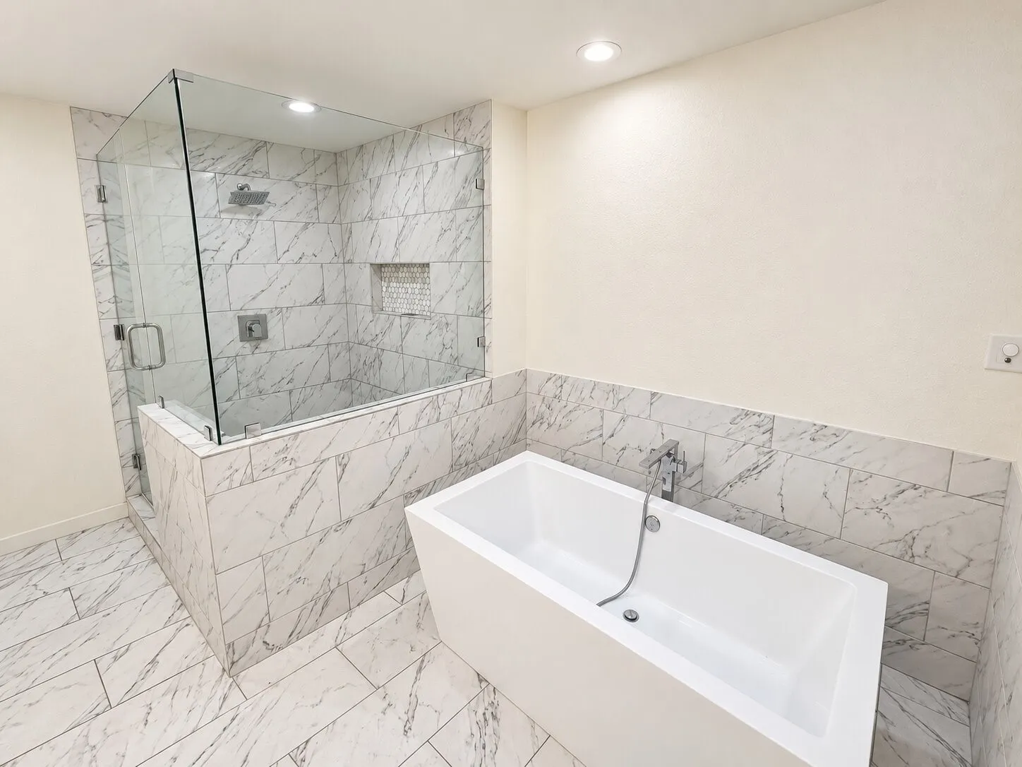 Freestanding soaking tub, walk-in shower with glass enclosure, rain showerhead, recessed lighting, and patterned tile flooring