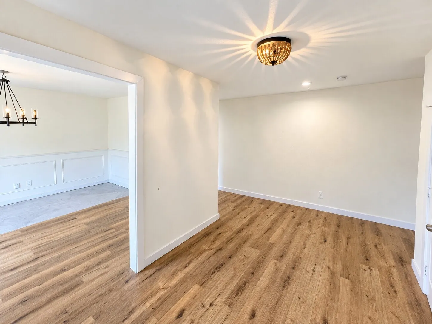 Spacious open floor plan with warm wood-finish flooring throughout, crisp white walls, and abundant natural light