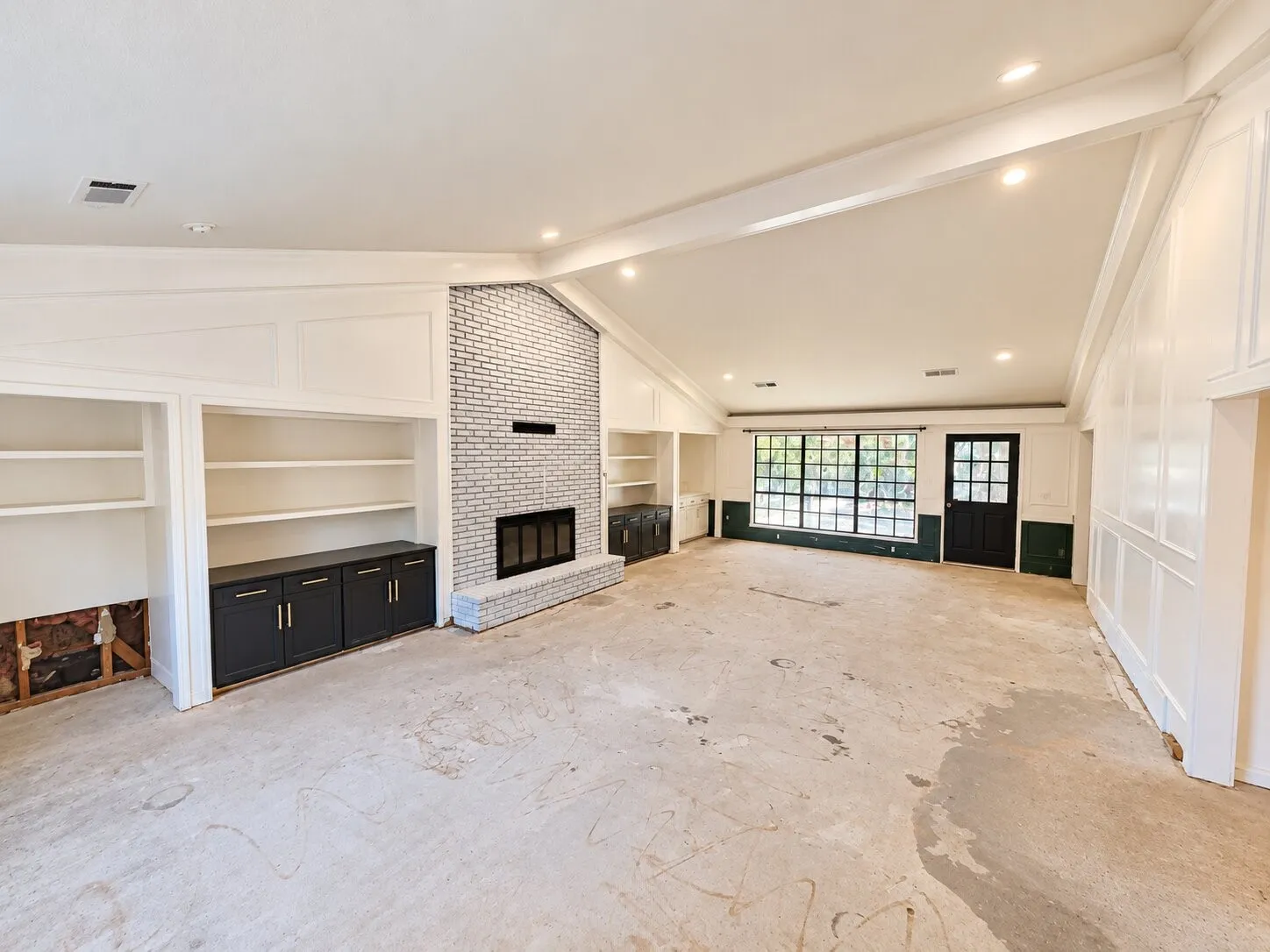 Vaulted ceiling with exposed beams, recessed lighting, painted brick fireplace, built-in shelving, and black grid-patterned window