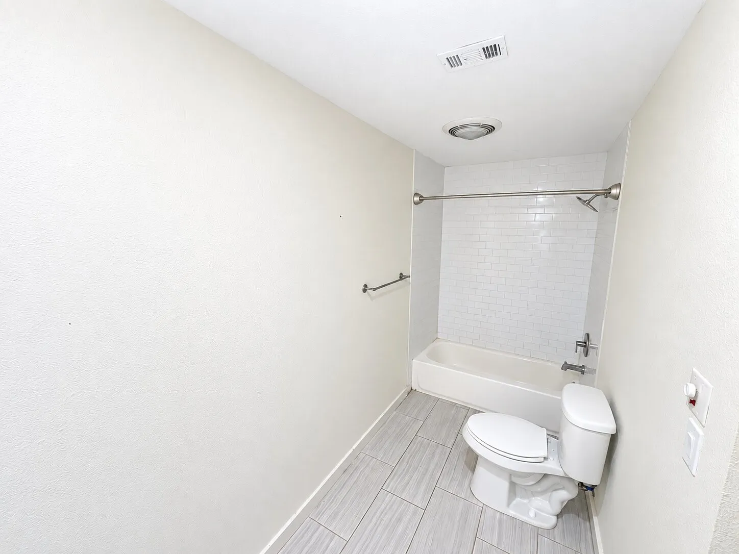 Bathroom featuring a white subway tile shower surround, a built-in bathtub, and light-toned tile flooring