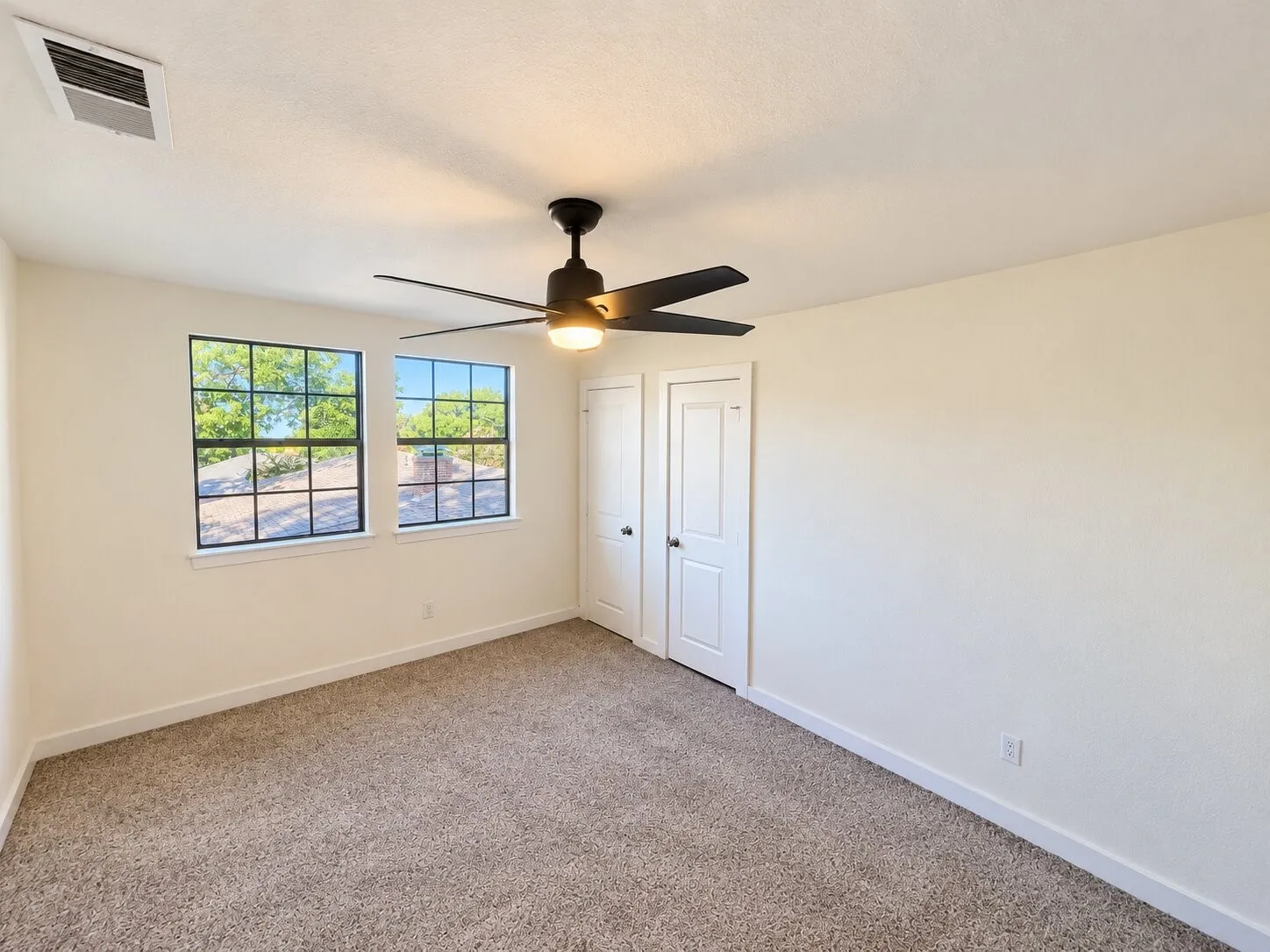 Plush carpet flooring, dual windows with dark trim, a ceiling fan with integrated lighting, and dual paneled doors