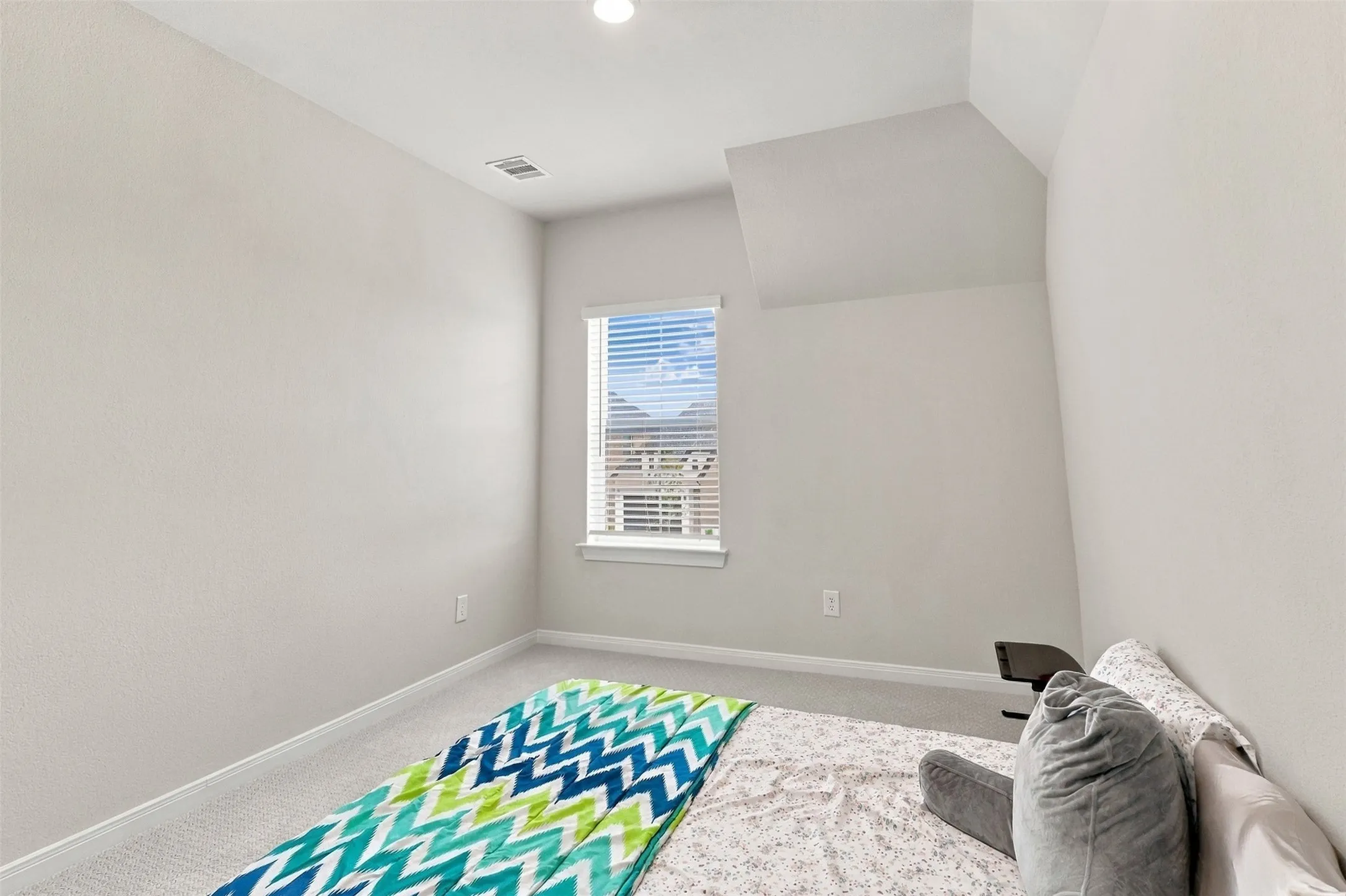 Recessed ceiling lighting, sloped ceiling detail, window with horizontal blinds, light-colored carpeting, neutral wall finish