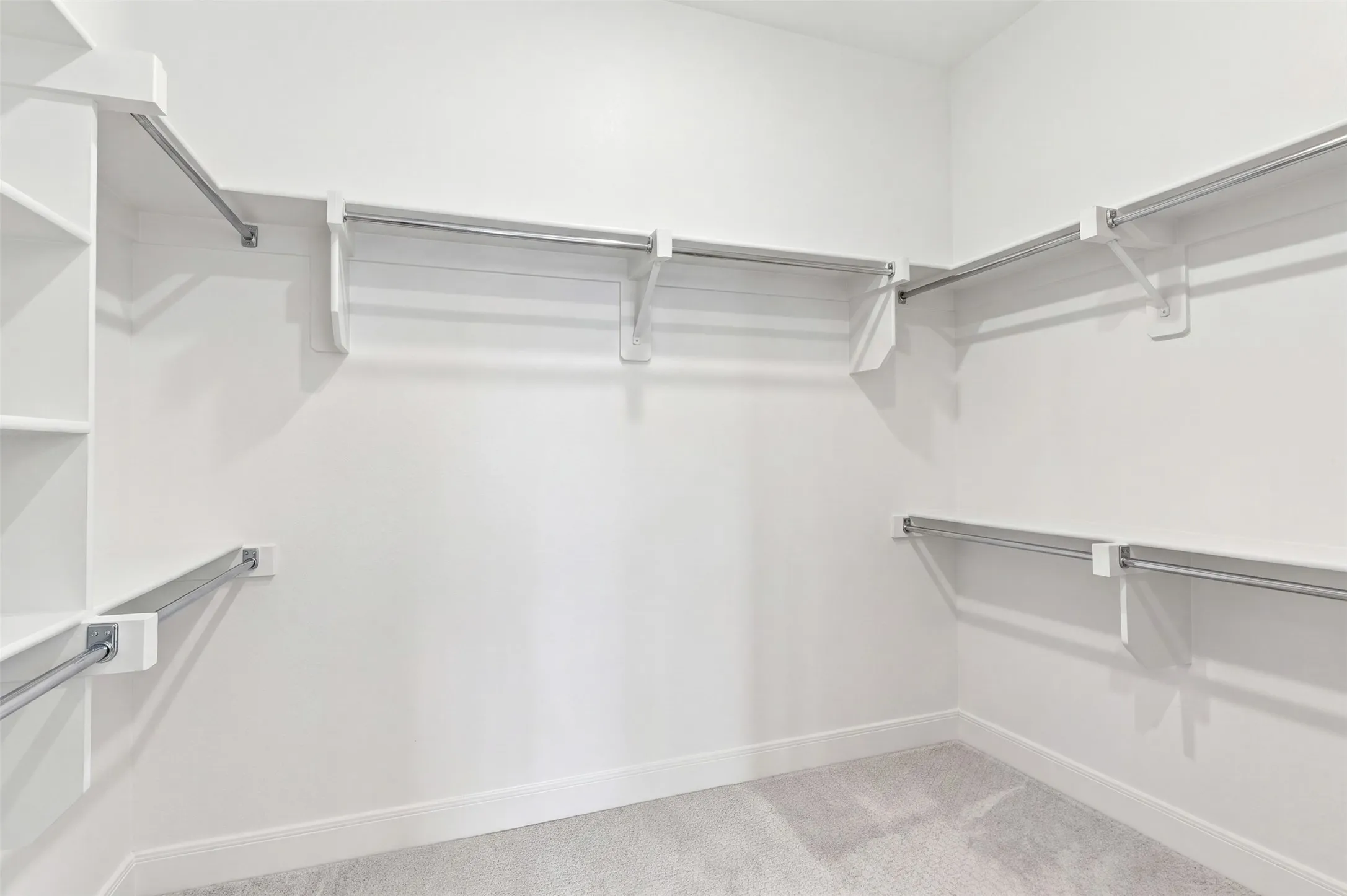 Spacious closet featuring white shelving, multiple hanging rods, and light-toned carpeting