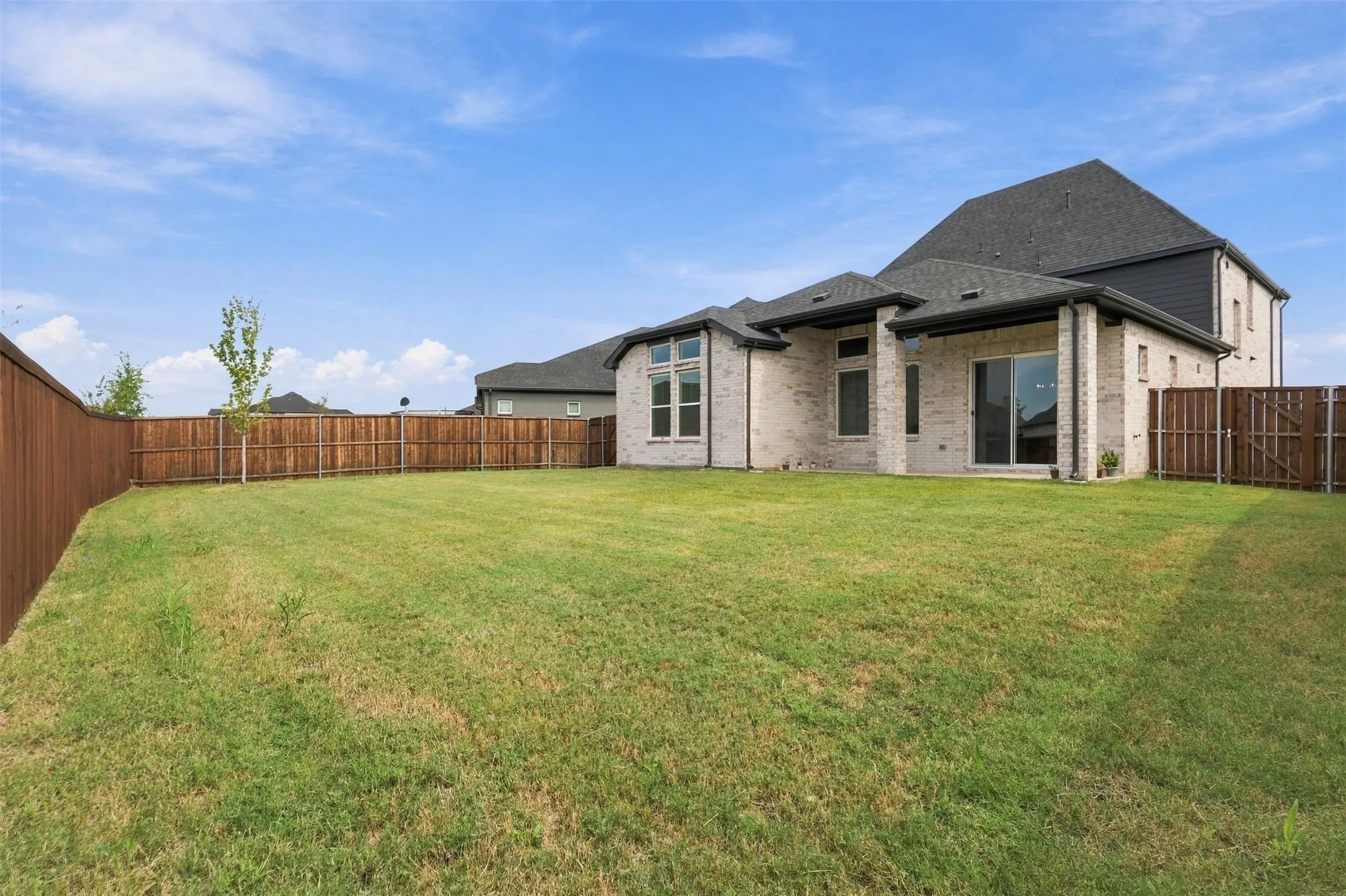 Expansive backyard featuring a manicured lawn, full privacy fencing, and a brick and siding exterior