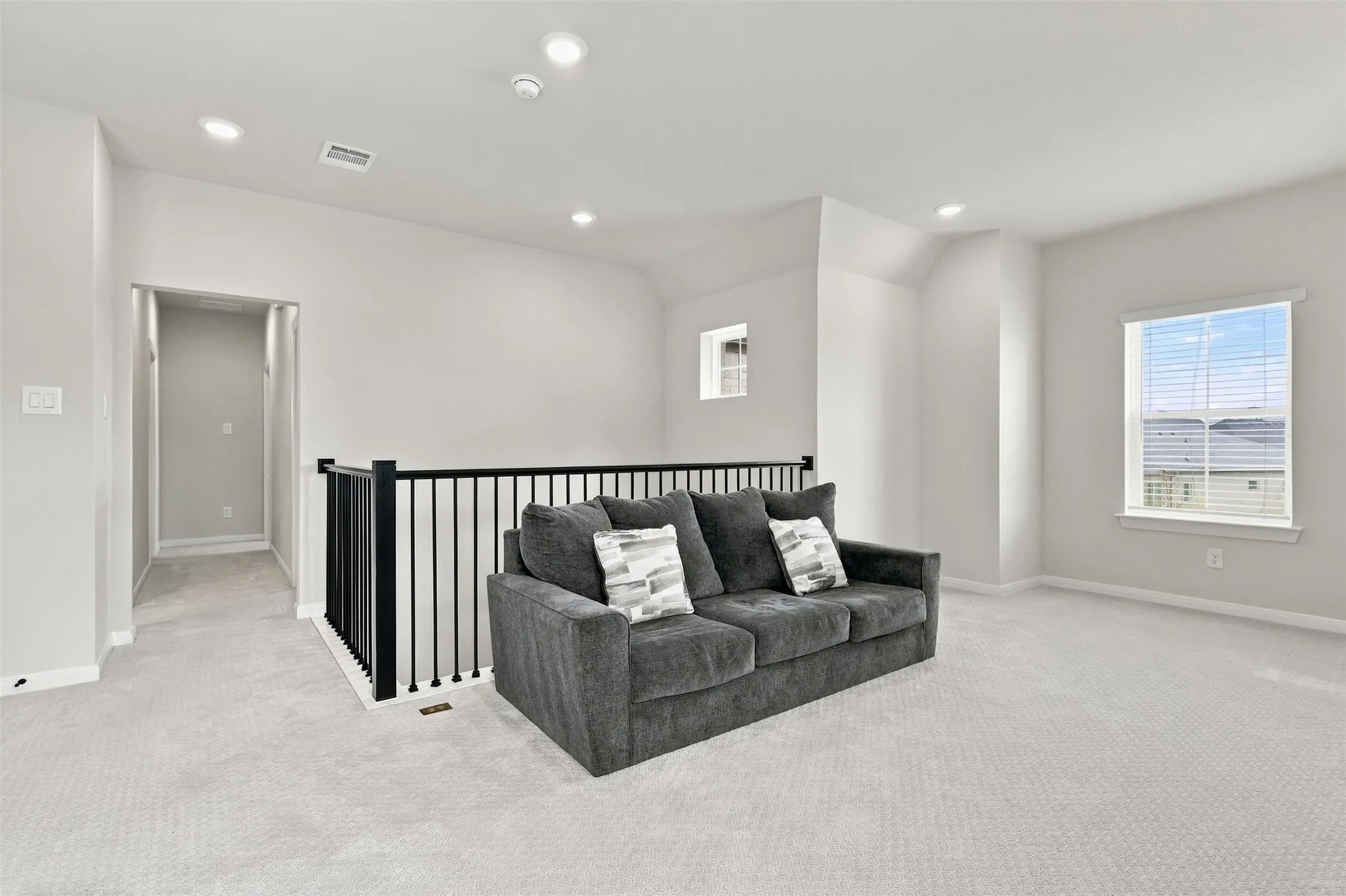 Carpeted loft area featuring a black metal railing, window with blinds, recessed lighting, and a neutral color palette