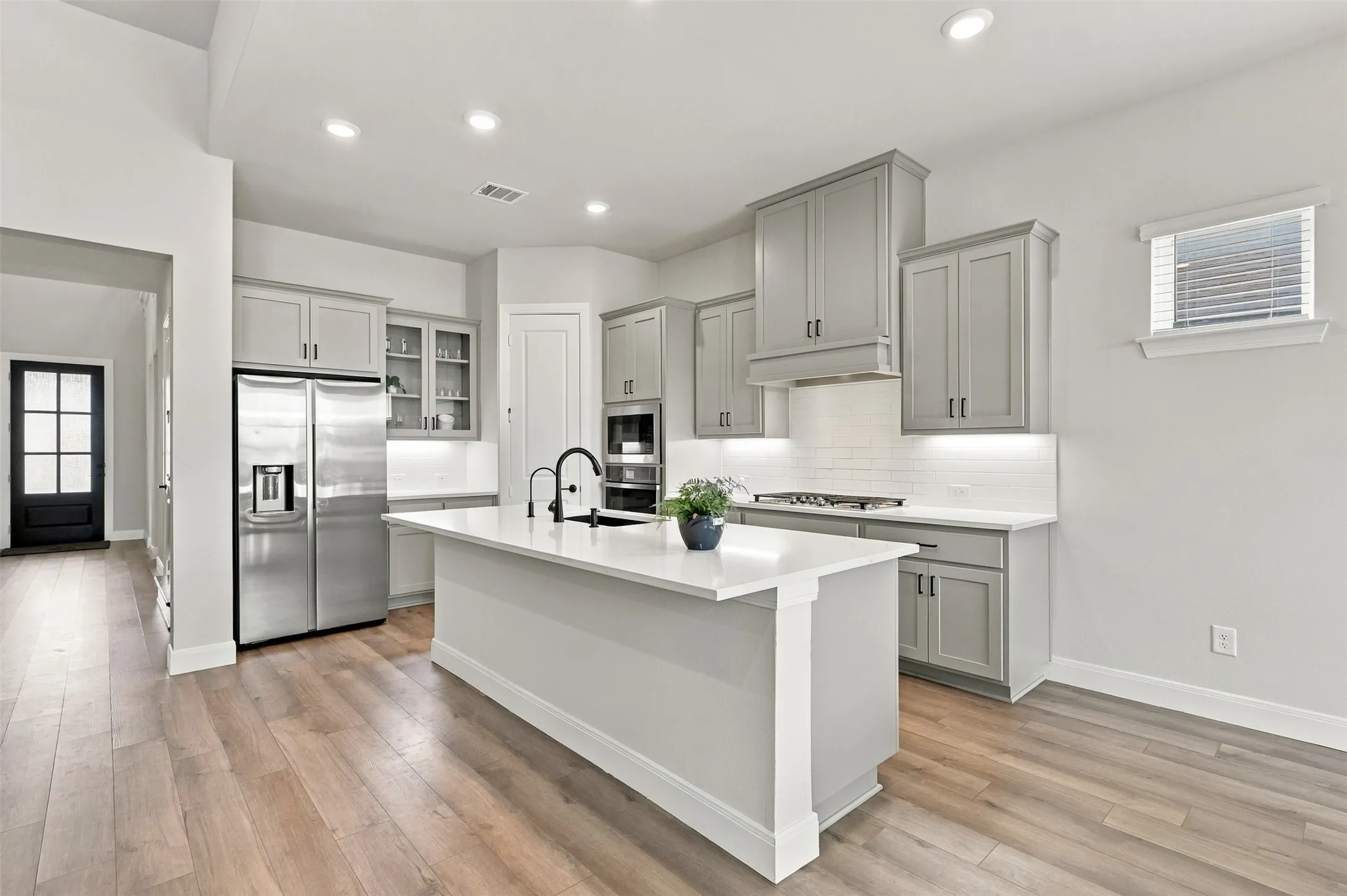 Spacious kitchen featuring an expansive central island, stainless steel appliances, recessed lighting, wood-finish flooring, and light gray​​‌​​​​‌​​‌‌​‌‌​​​‌‌​‌​‌​‌​​​‌​​ cabinetry