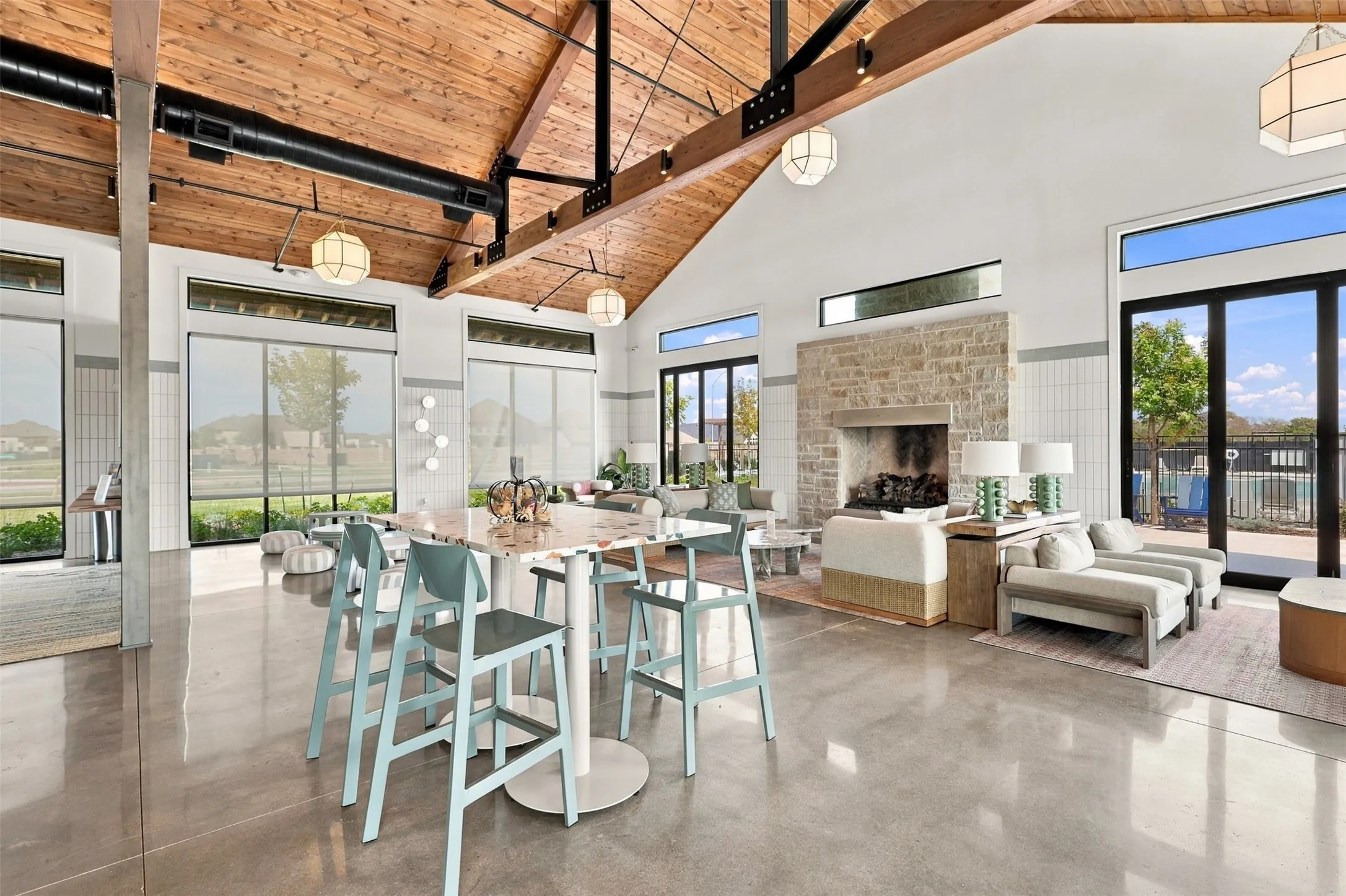 Vaulted wood plank ceiling with exposed beams, stone-clad fireplace, polished concrete flooring, extensive window walls, and transom windows