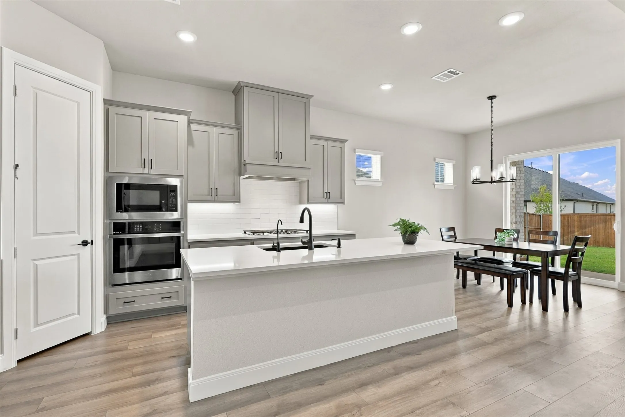 Kitchen featuring gray cabinetry, stainless steel appliances, a white tile backsplash, and a central island with a white countertop