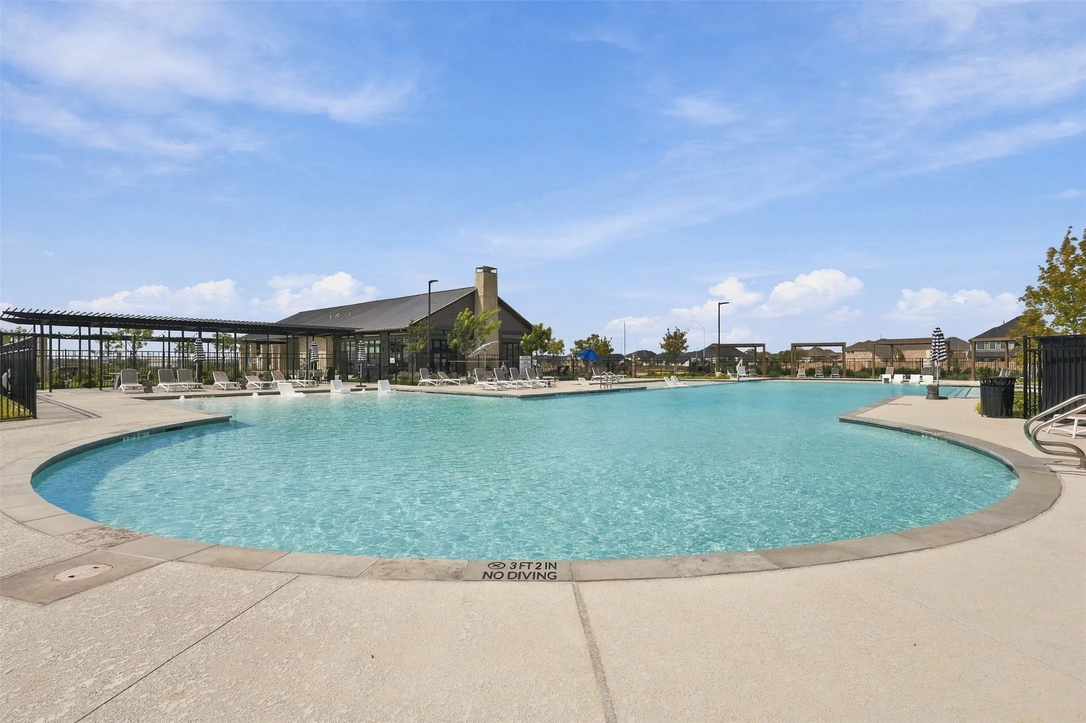 Expansive outdoor pool with integrated water features, surrounding concrete decking, and a modern clubhouse with an attached pergola structure