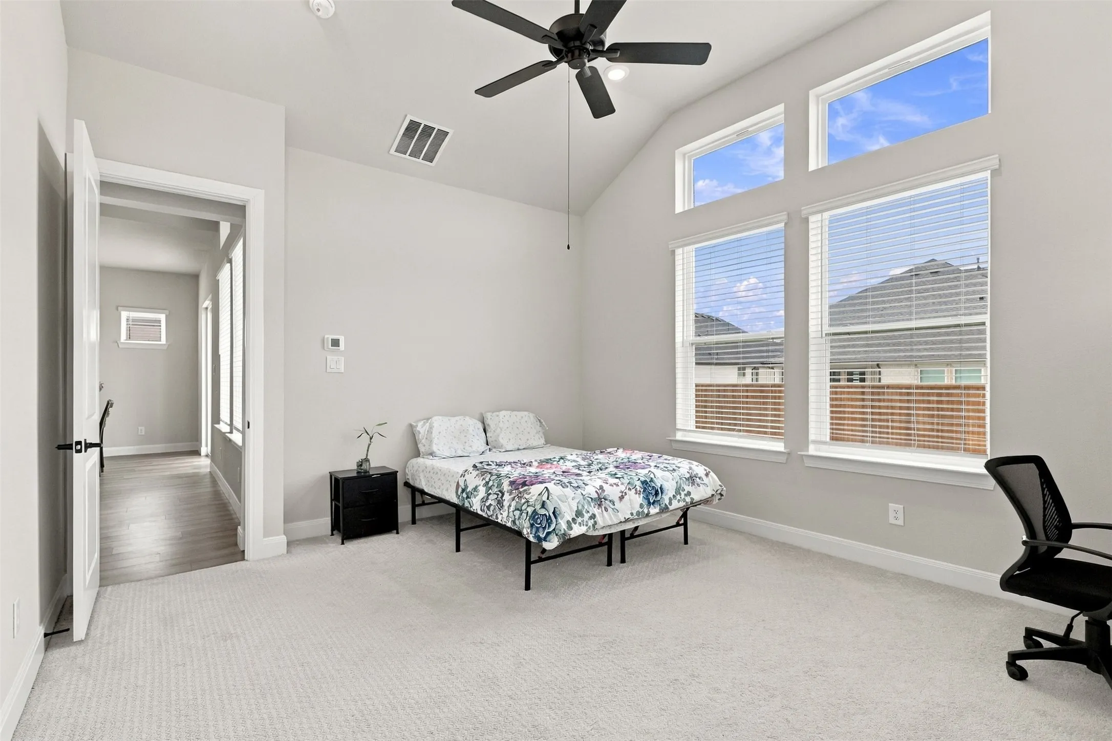 Vaulted ceiling, multiple large windows, ceiling fan, neutral wall tones, and plush carpet flooring