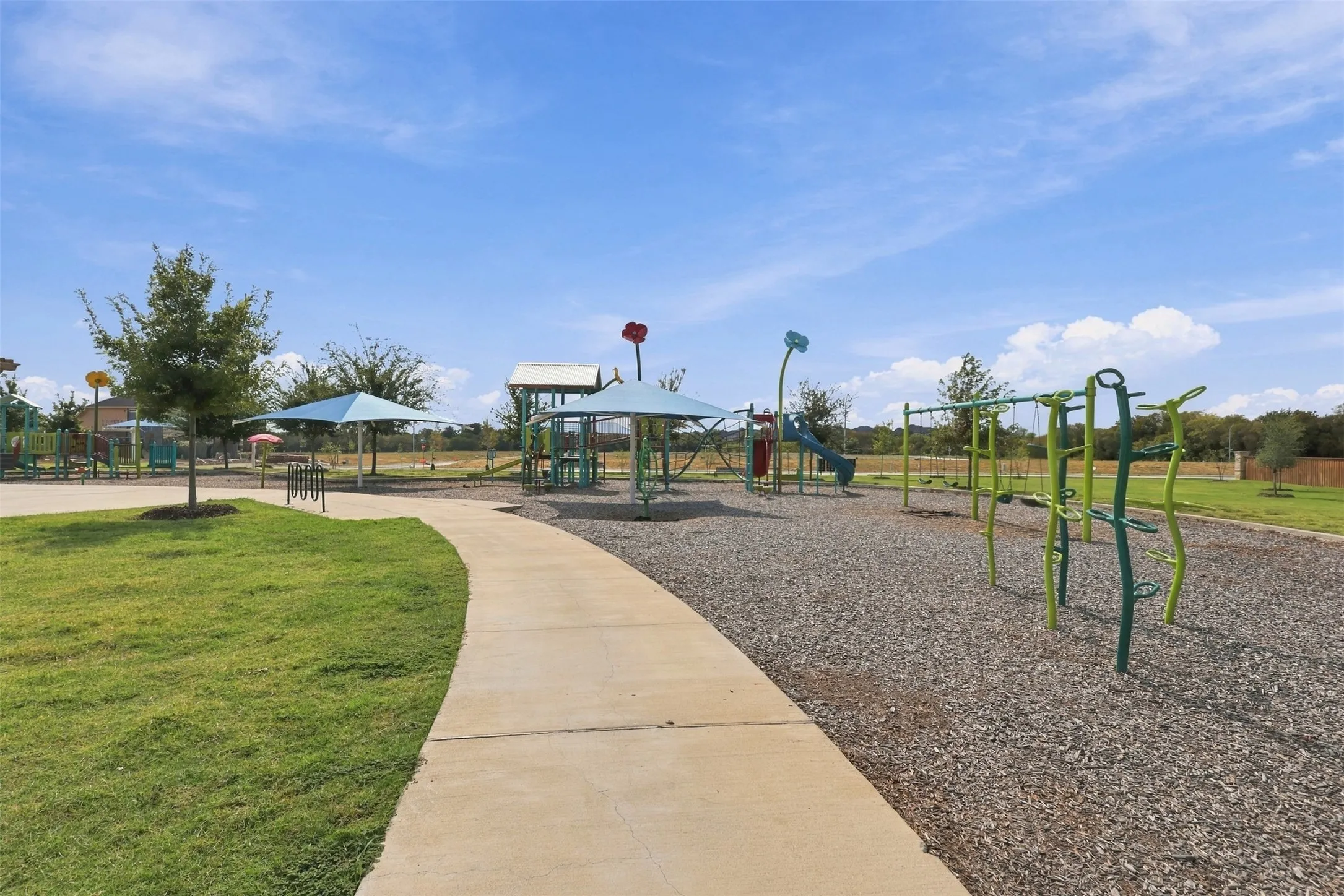 Manicured lawn area with a concrete pathway, shaded playground structures, and a separate swing set area