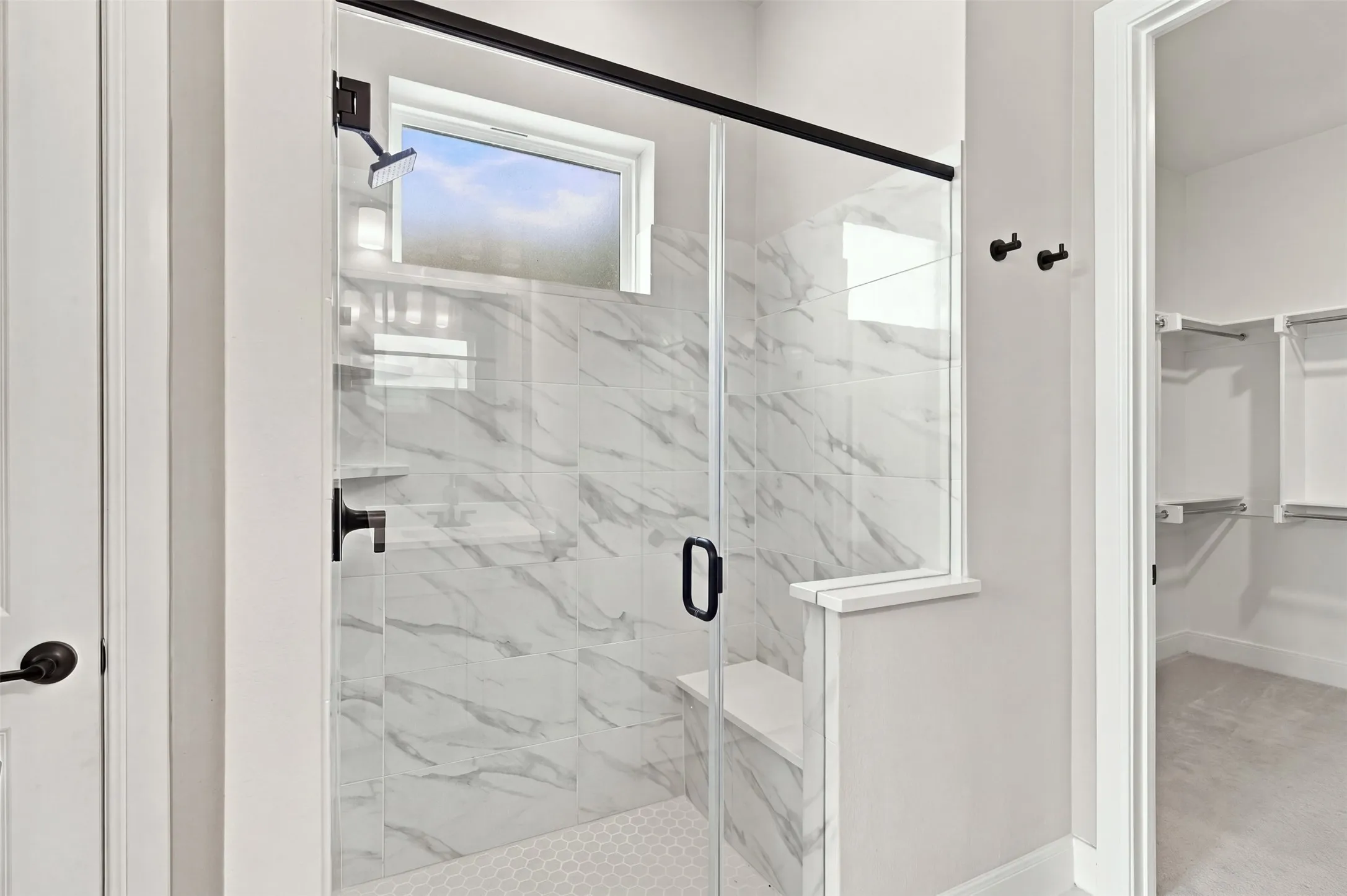Walk-in shower with clear glass enclosure and black hardware, featuring marble-style wall tiling, a built-in bench, and a hexagonal floor tile pattern