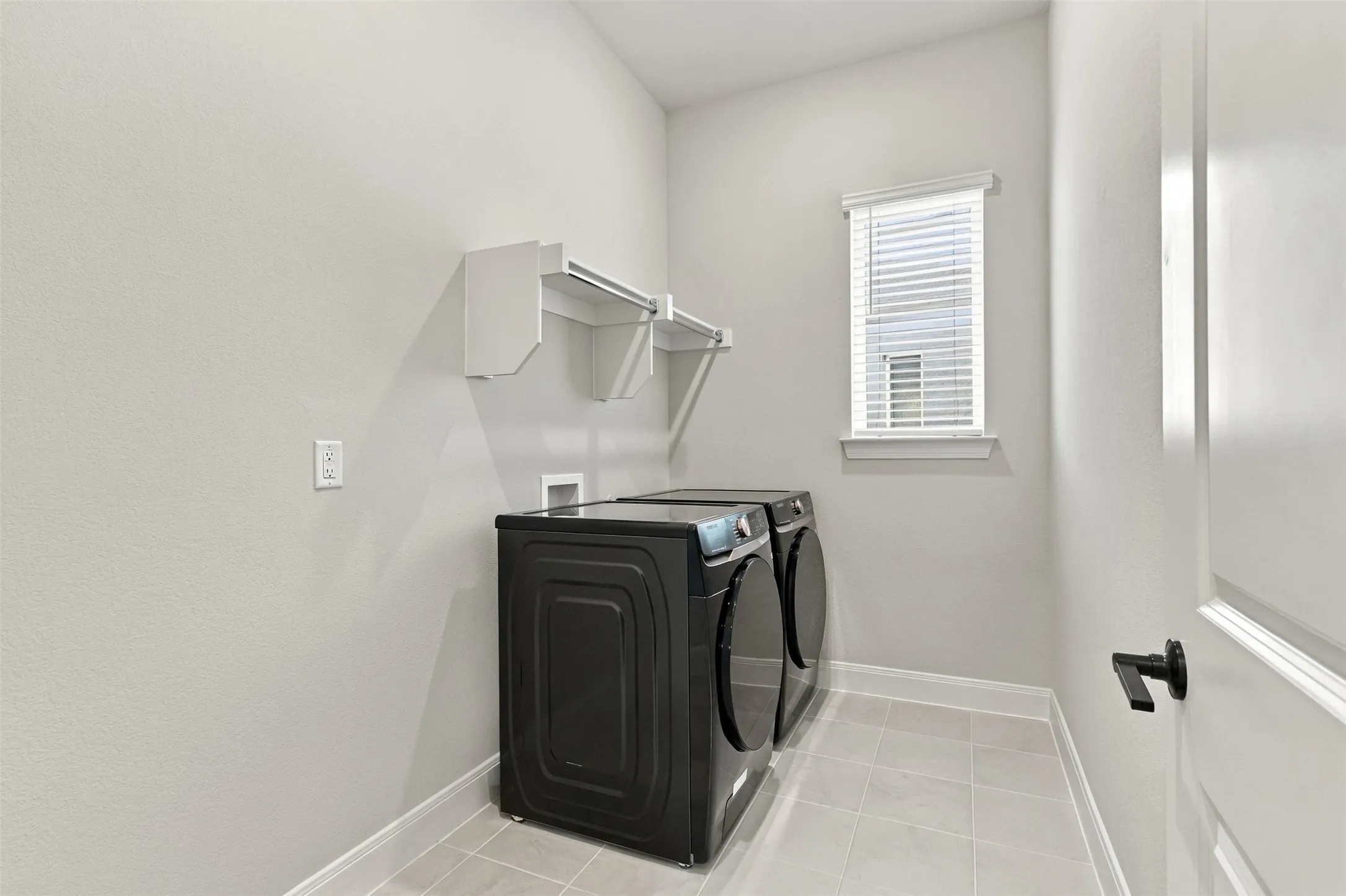 Laundry area featuring a window, built-in shelving, tiled flooring, and a white paneled door with matte black hardware