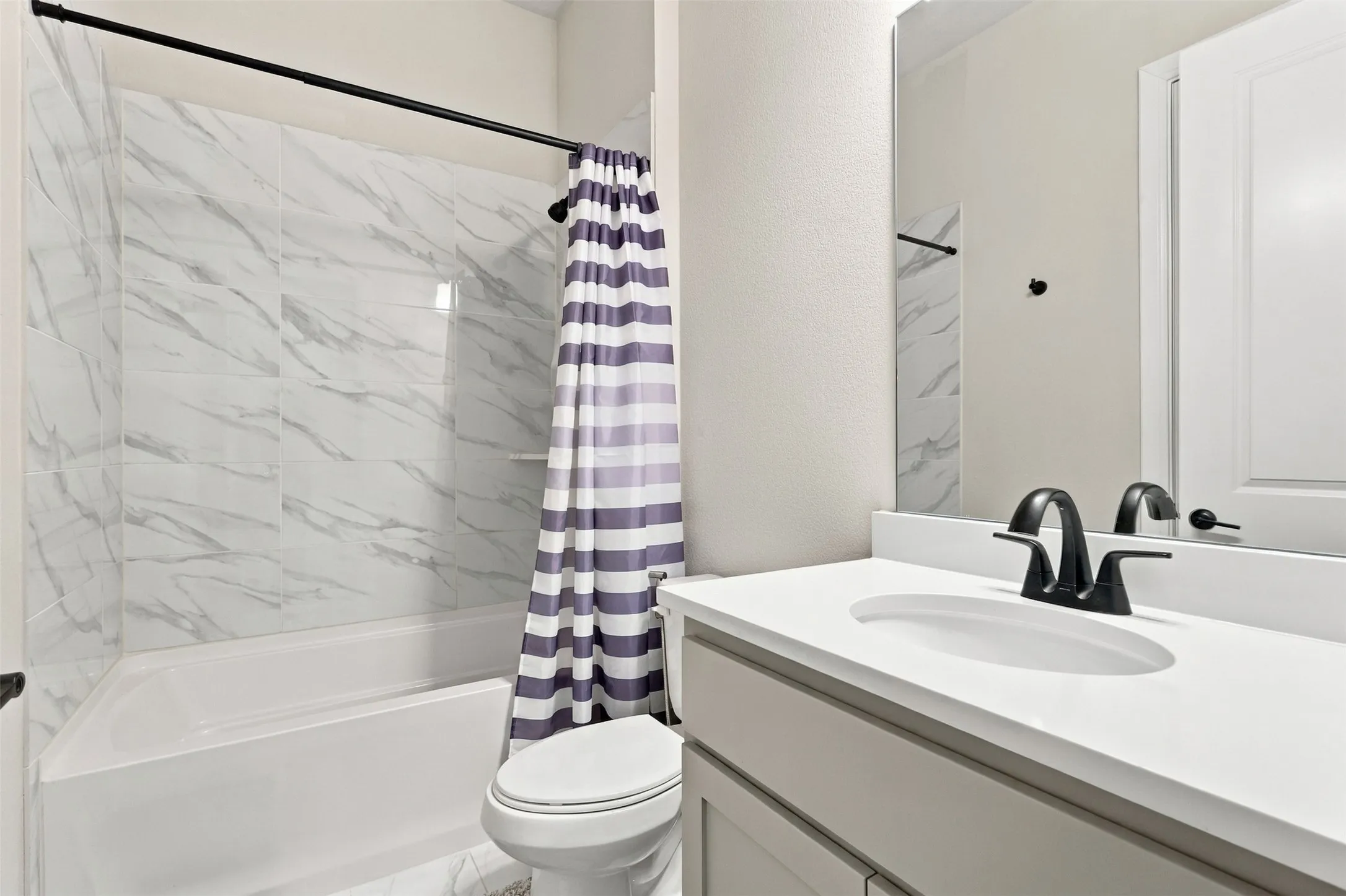 Bathtub with marble-look tile surround, single vanity with integrated sink, matte black faucet, and frameless mirror